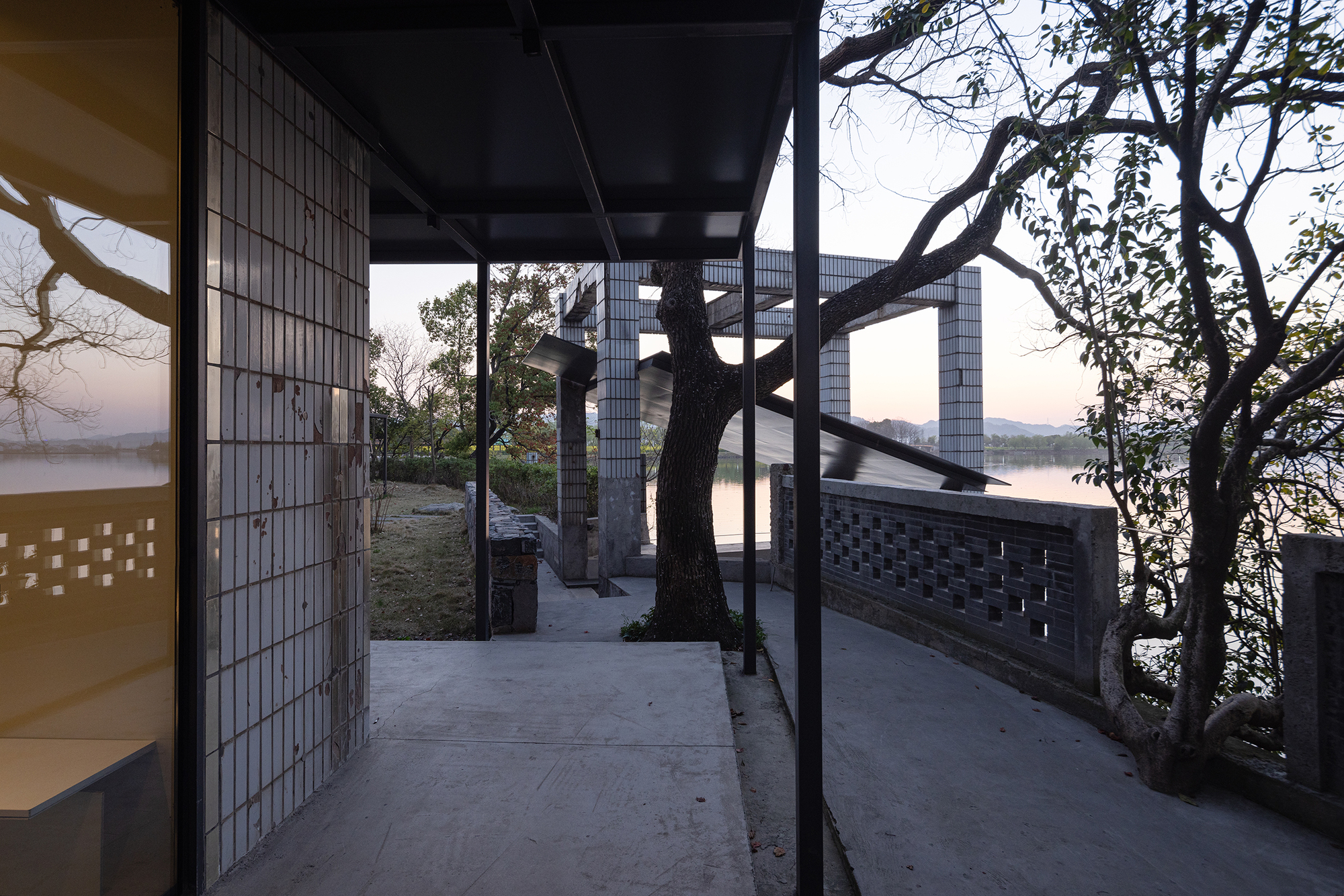 Exterior terrace framed by steel columns and glass block walls with preserved trees at dusk