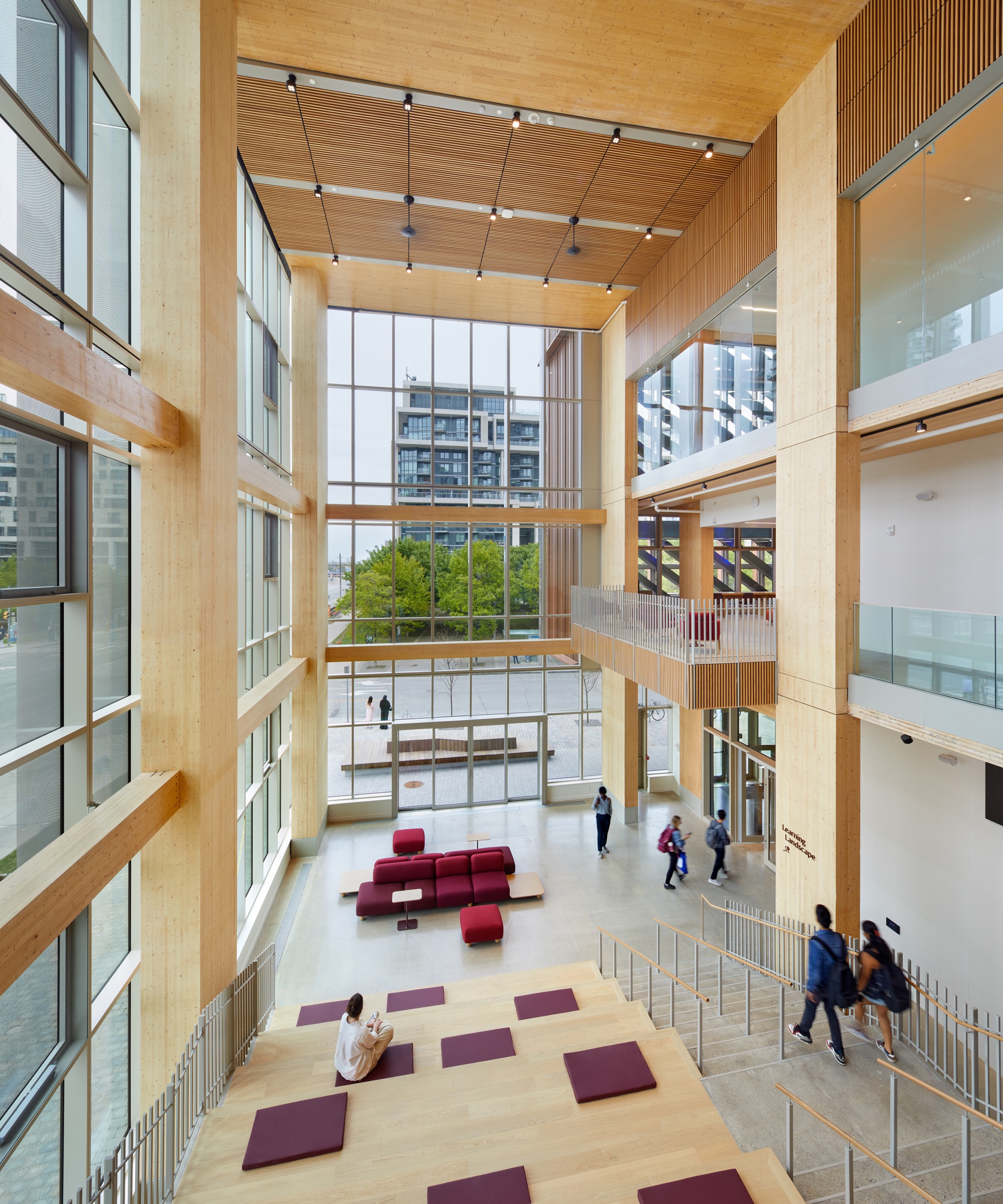 Multi-story atrium with exposed timber beams and ceiling panels overlooking people scattered below