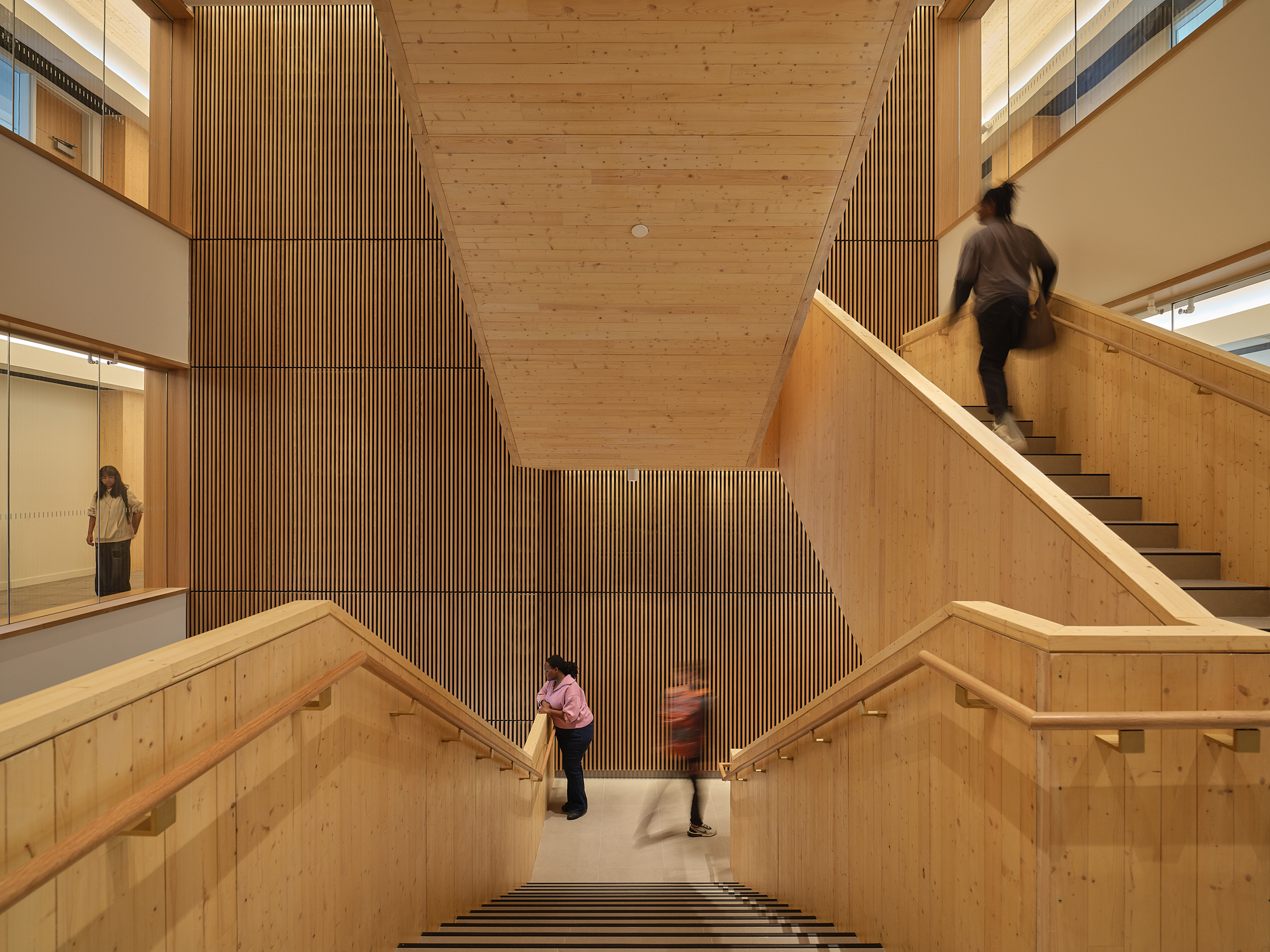 View down the timber-clad stairwell with vertical slatted wall as people ascend and descend