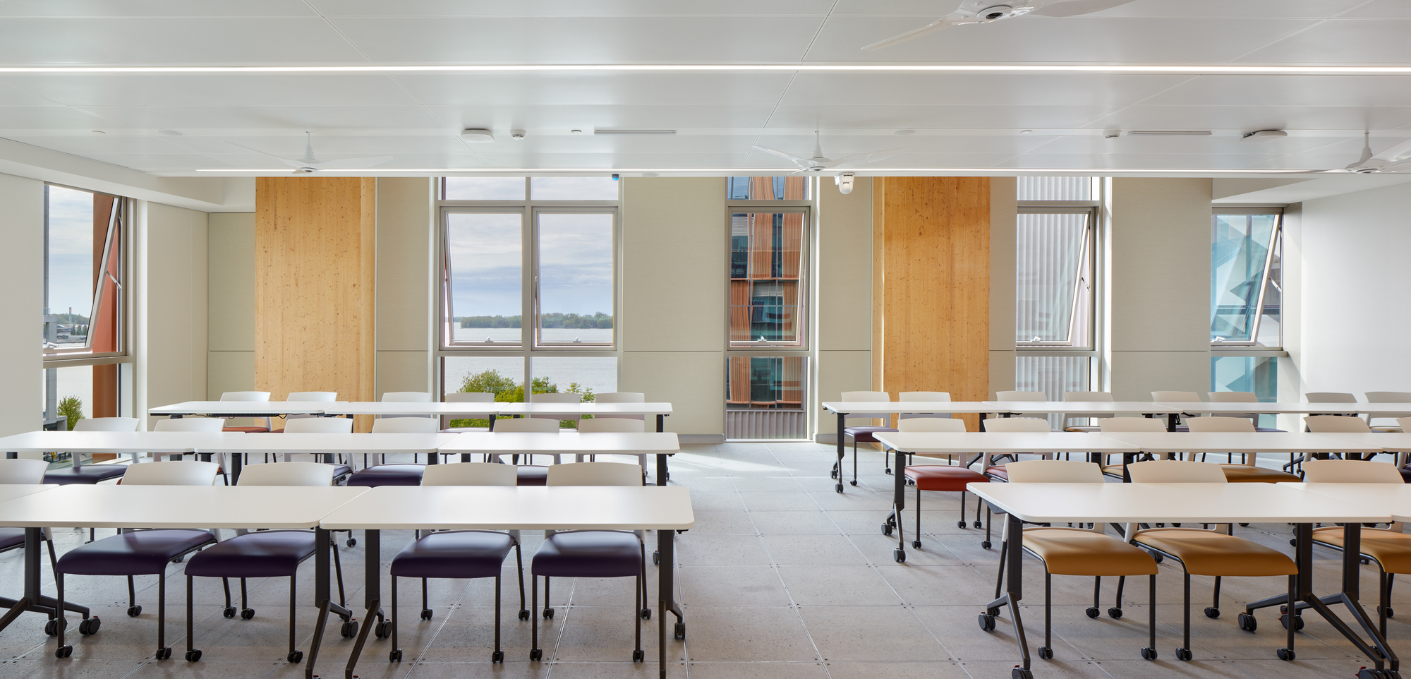 Classroom interior with movable white tables arranged in rows beneath linear ceiling lights and operable windows