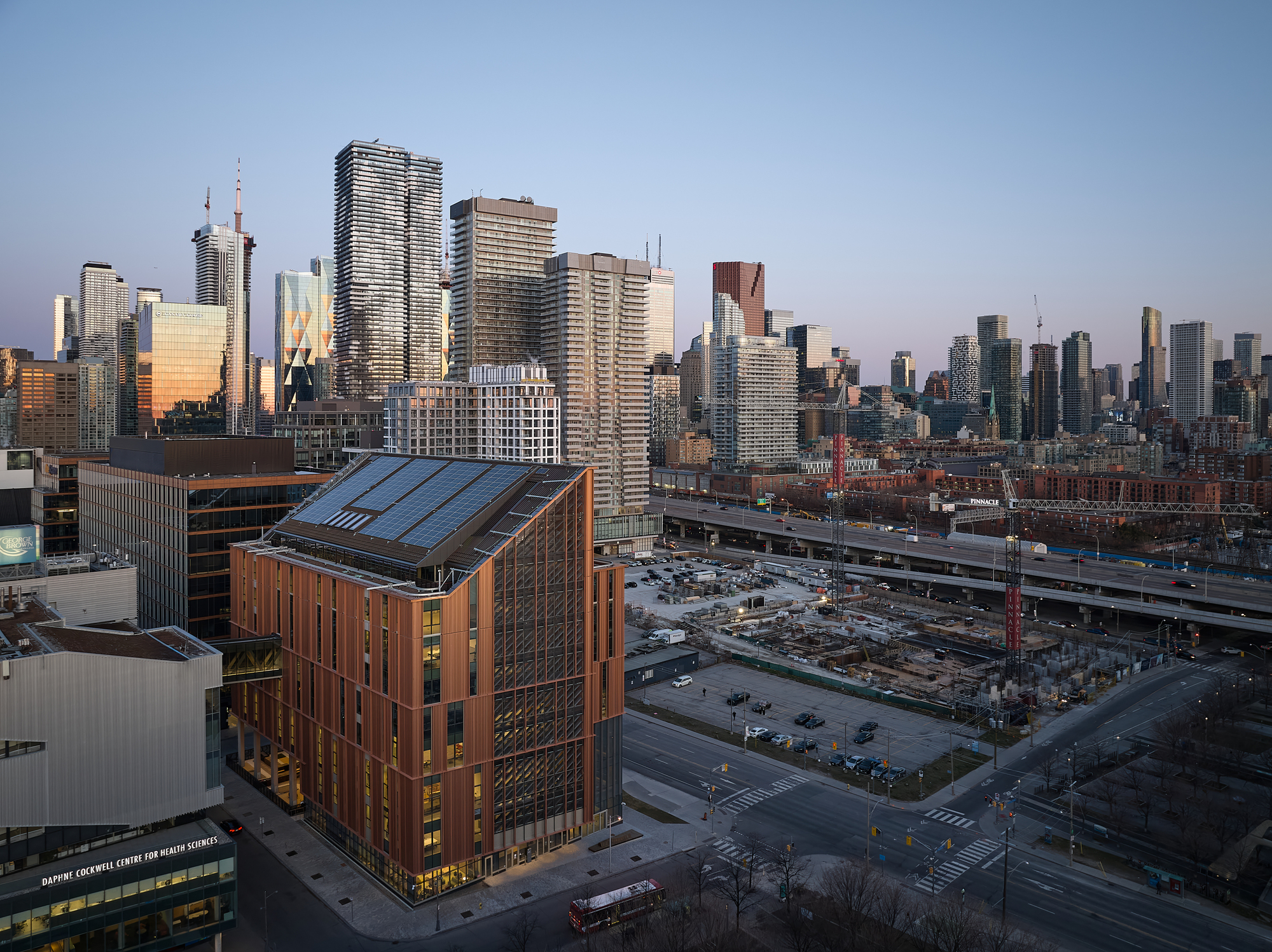 Rooftop view showing the angled solar panel array atop the copper-wrapped volume against the city skyline