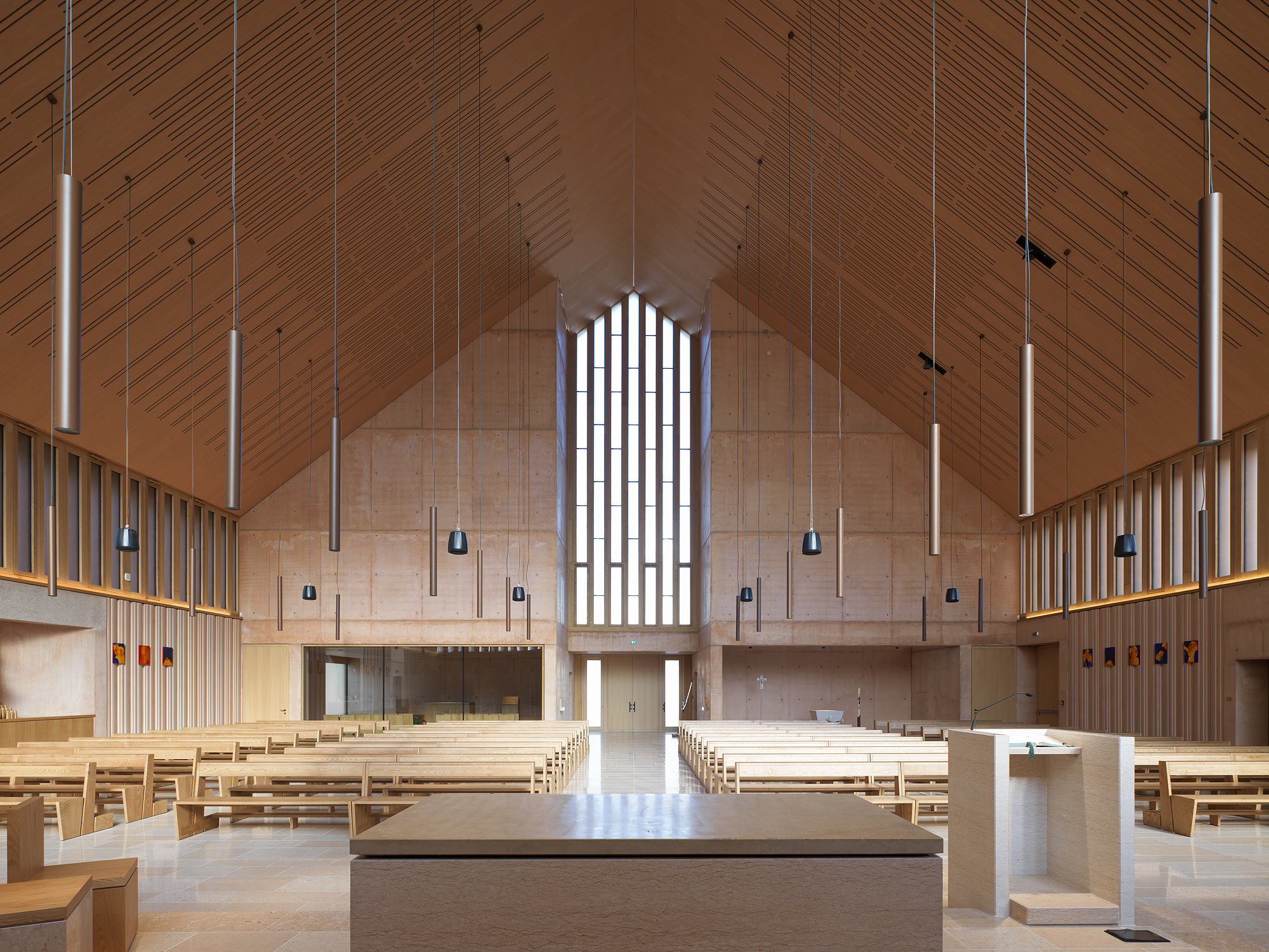 Interior sanctuary with timber-clad pitched ceiling, pendant lights and an arched window above the altar