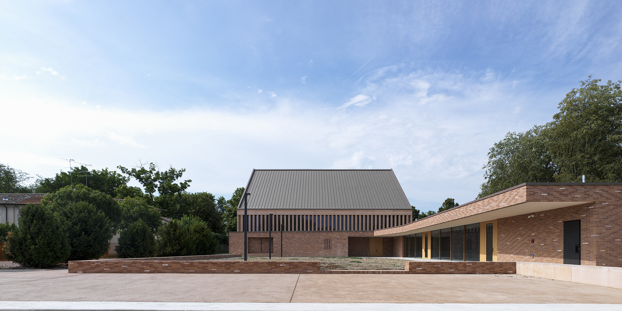 Side view of the gabled roof and low brick wings surrounded by trees under cloud