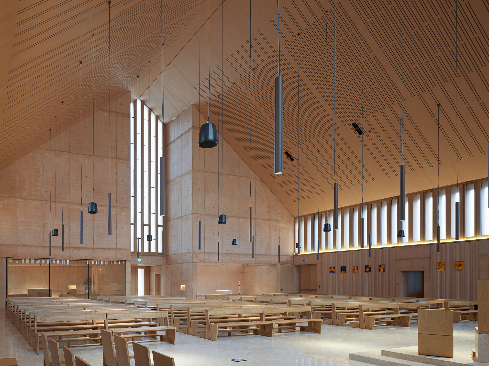 Interior sanctuary with timber ceiling, vertical light slots, suspended pendants and rows of wooden pews