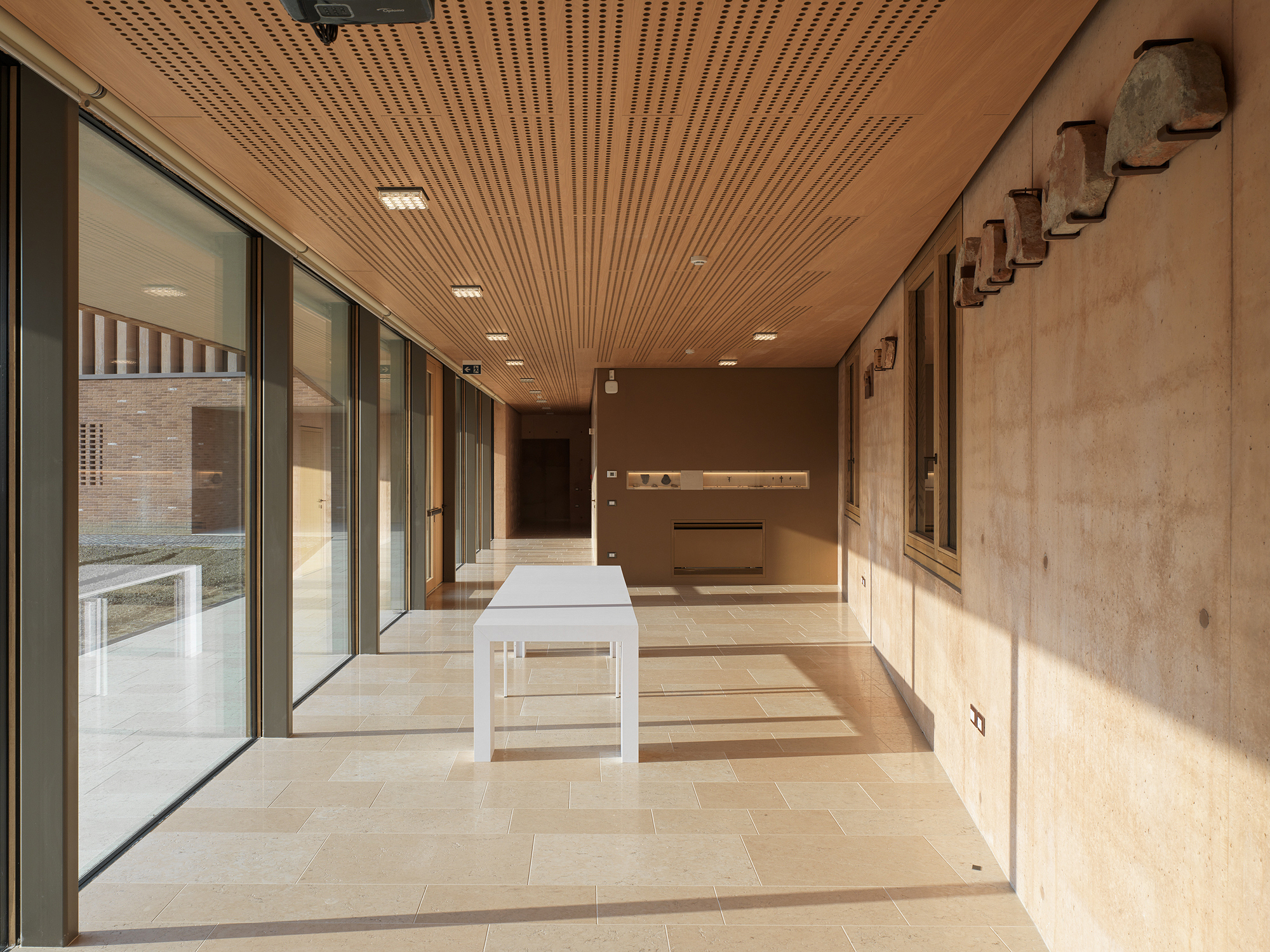 Covered corridor with slatted wood ceiling, glazed walls and limestone flooring in afternoon light