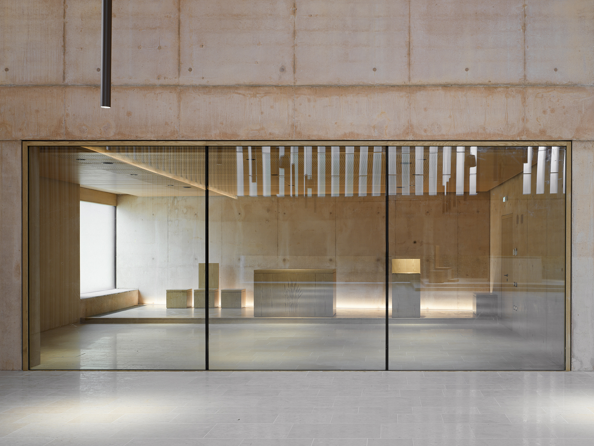 Glass partition framing view into sanctuary with concrete walls and uplighting beneath altar platform
