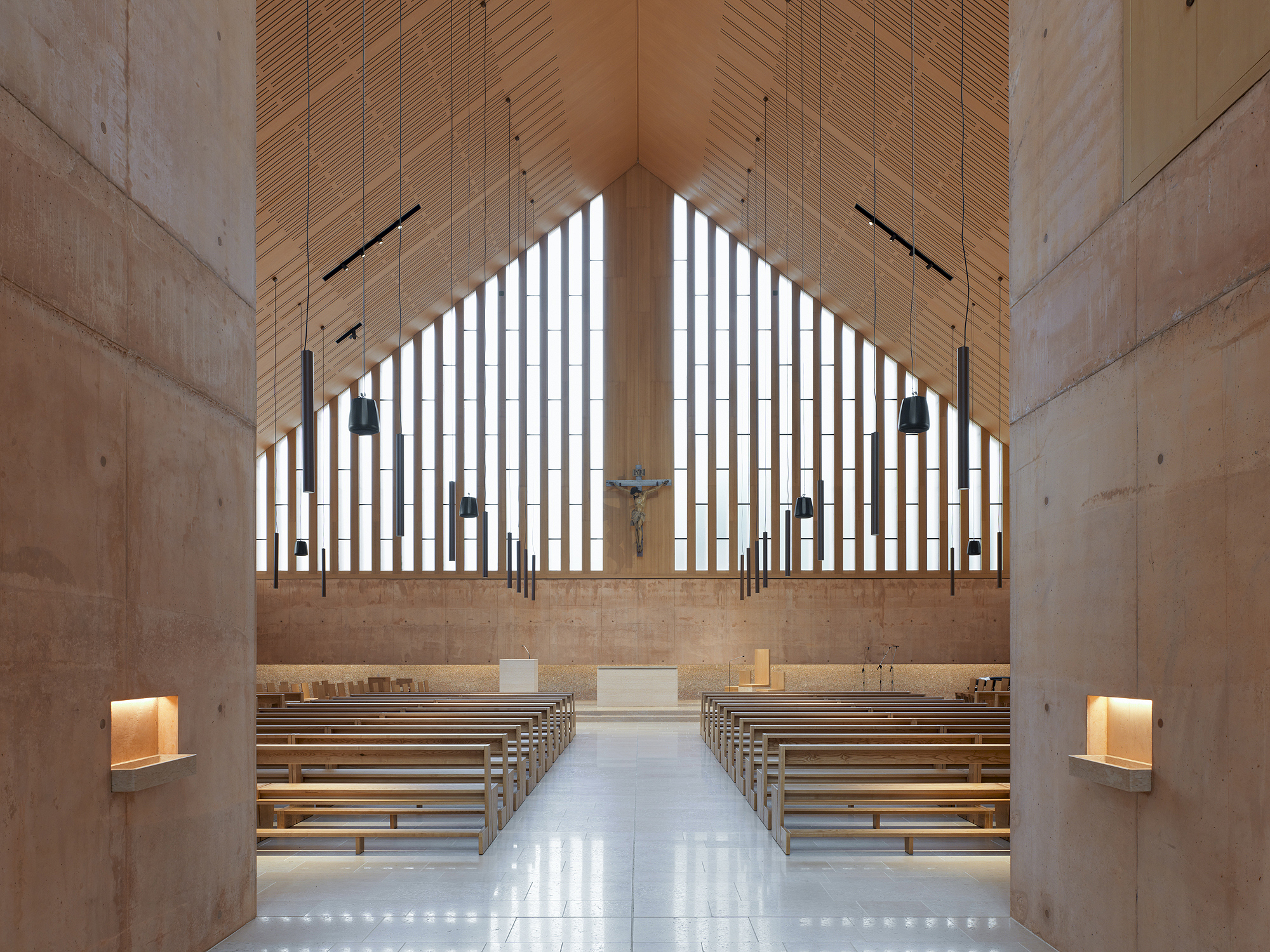 Sanctuary interior with wooden pews facing a vertical slatted window wall and timber ceiling panels
