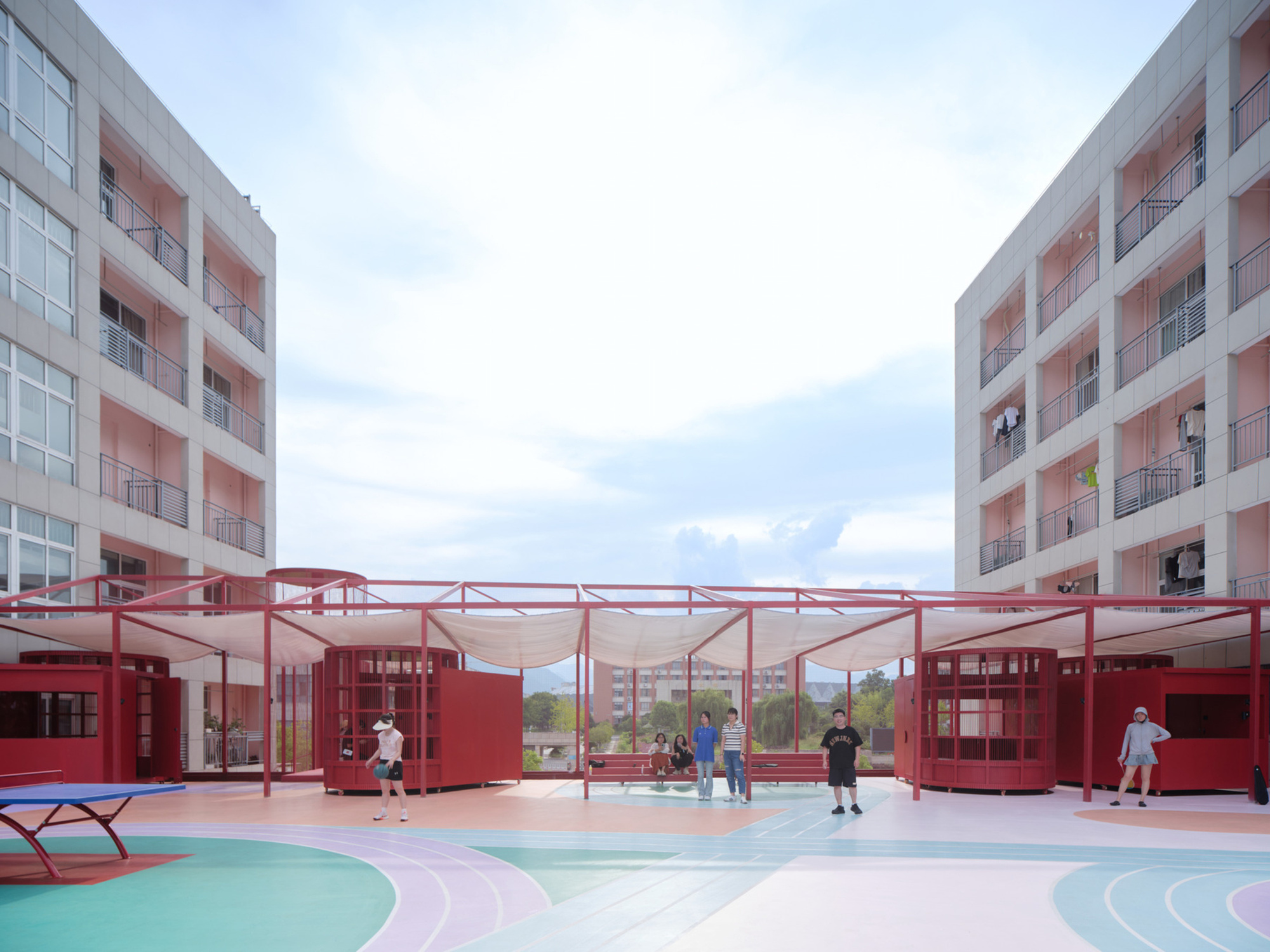 Courtyard with red steel canopy structure and modular volumes between residential blocks with children playing