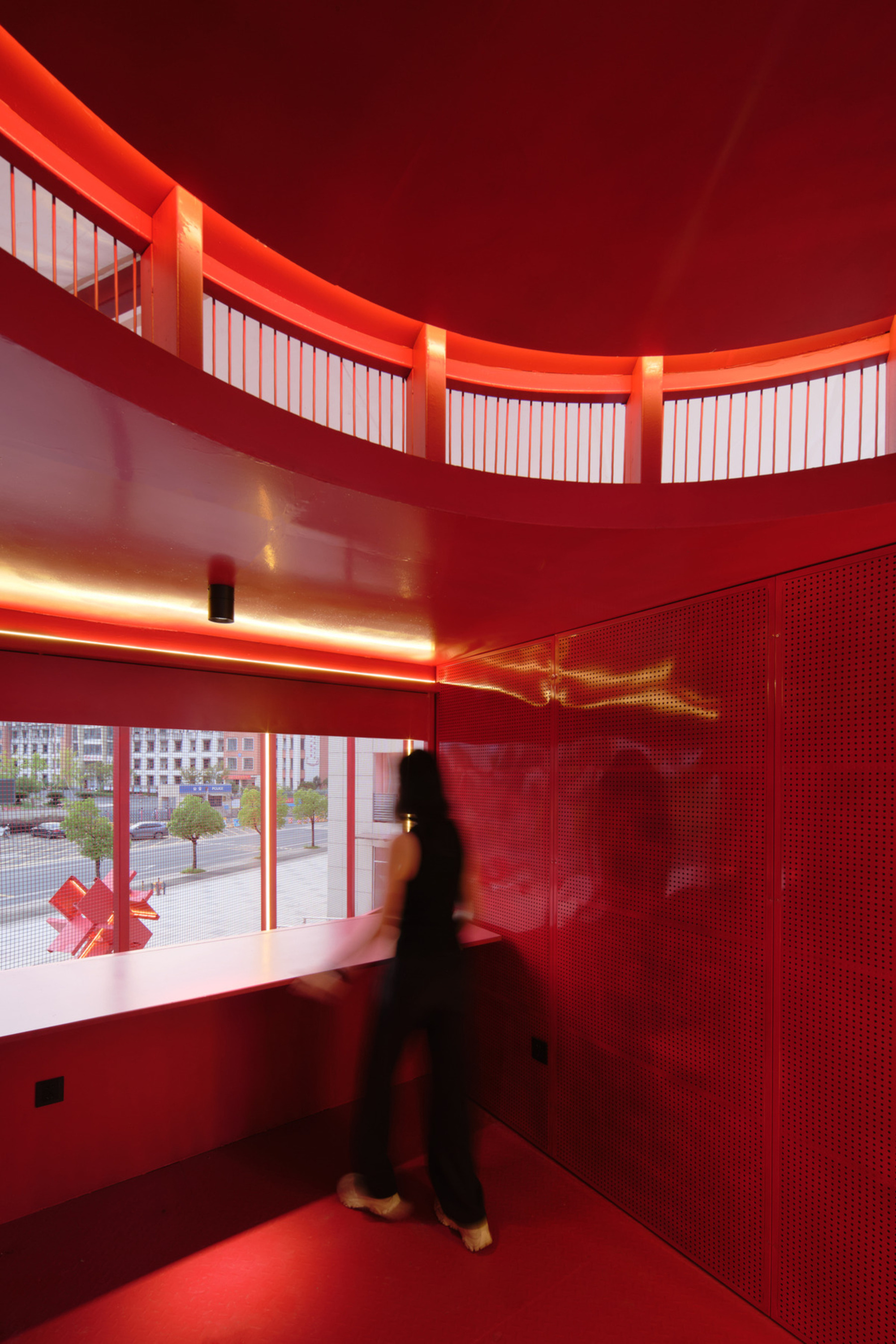 Red interior space with curved clerestory windows and a figure walking past perforated wall panels