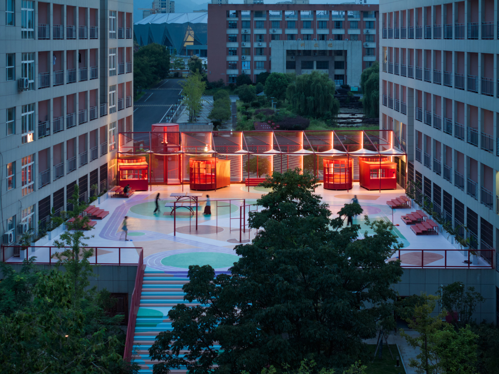 Aerial view of illuminated red pavilion with sawtooth roof on rooftop courtyard at dusk