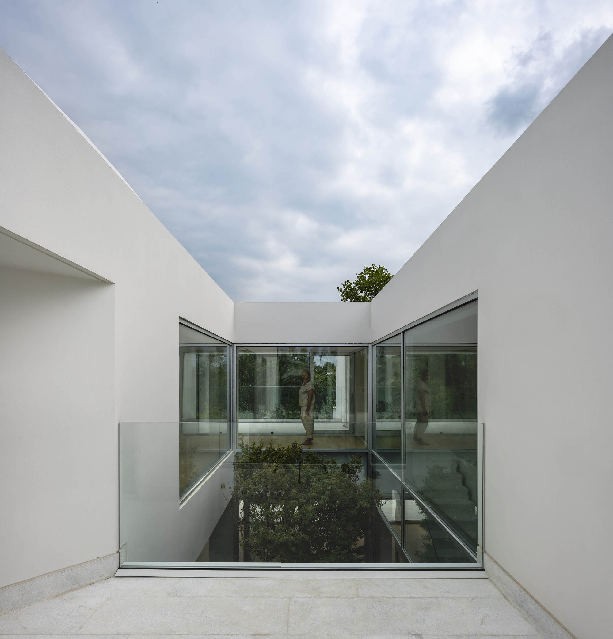 Glass-floored bridge spanning the sunken courtyard between white rendered walls open to the sky