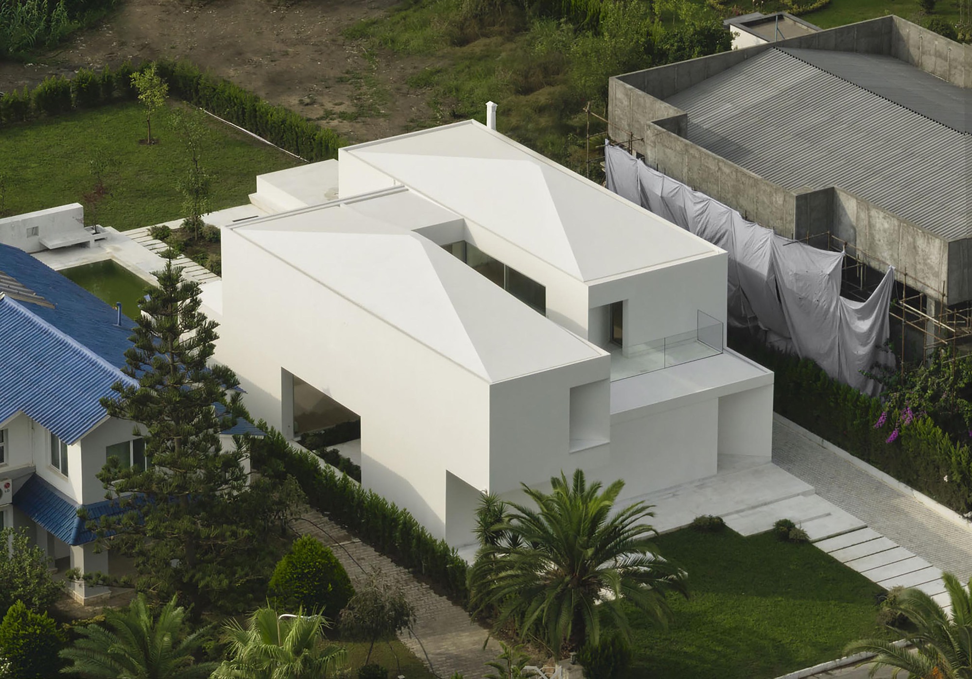 Drone view showing the folded roof planes above interlocking white volumes surrounded by palm trees