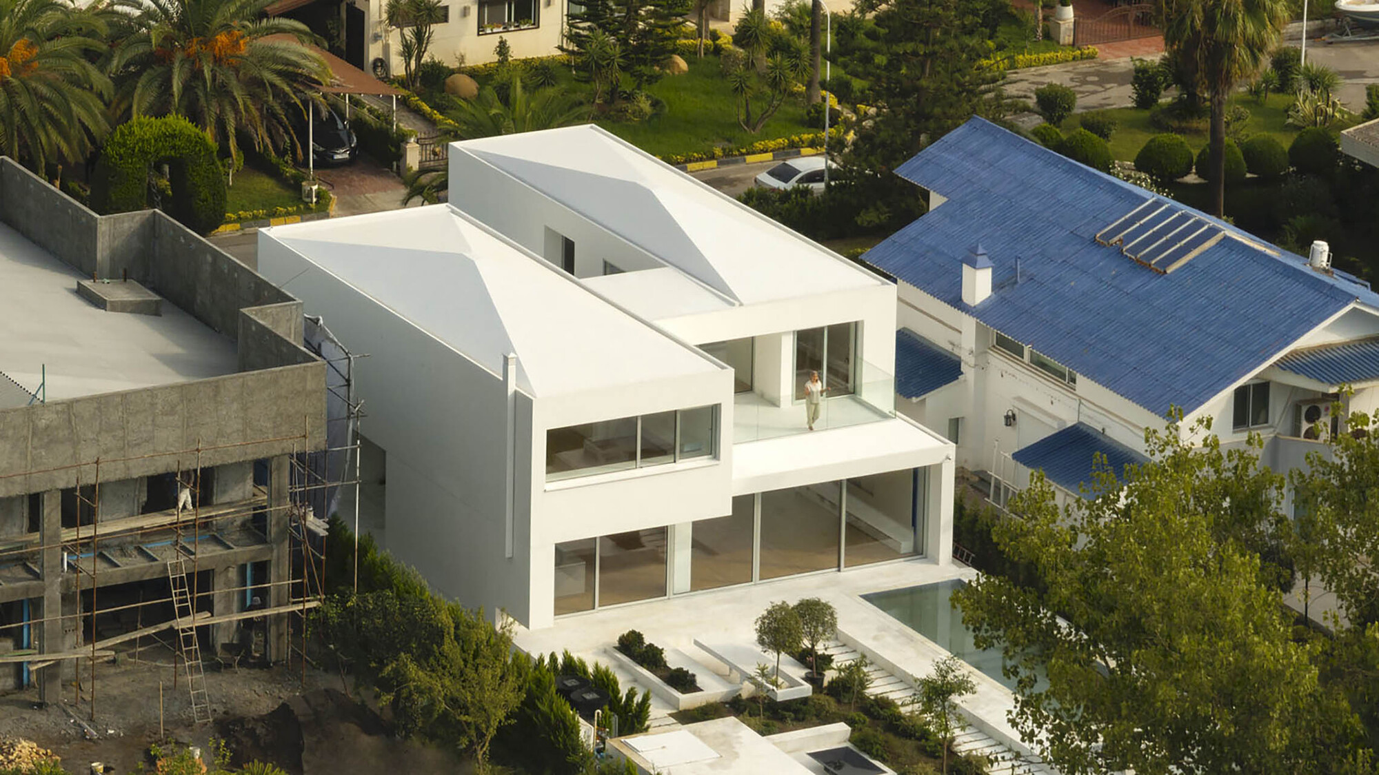 Elevated view of the white stucco facade with ribbon windows and asymmetric roof forms among palm trees