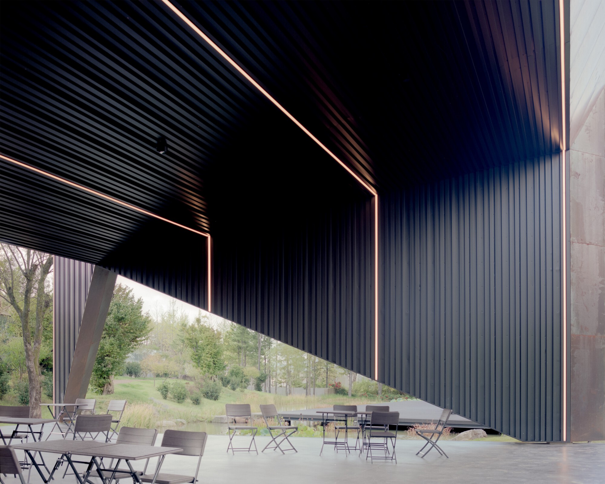 Covered terrace with corrugated metal ceiling and angled columns framing a lawn and distant hills
