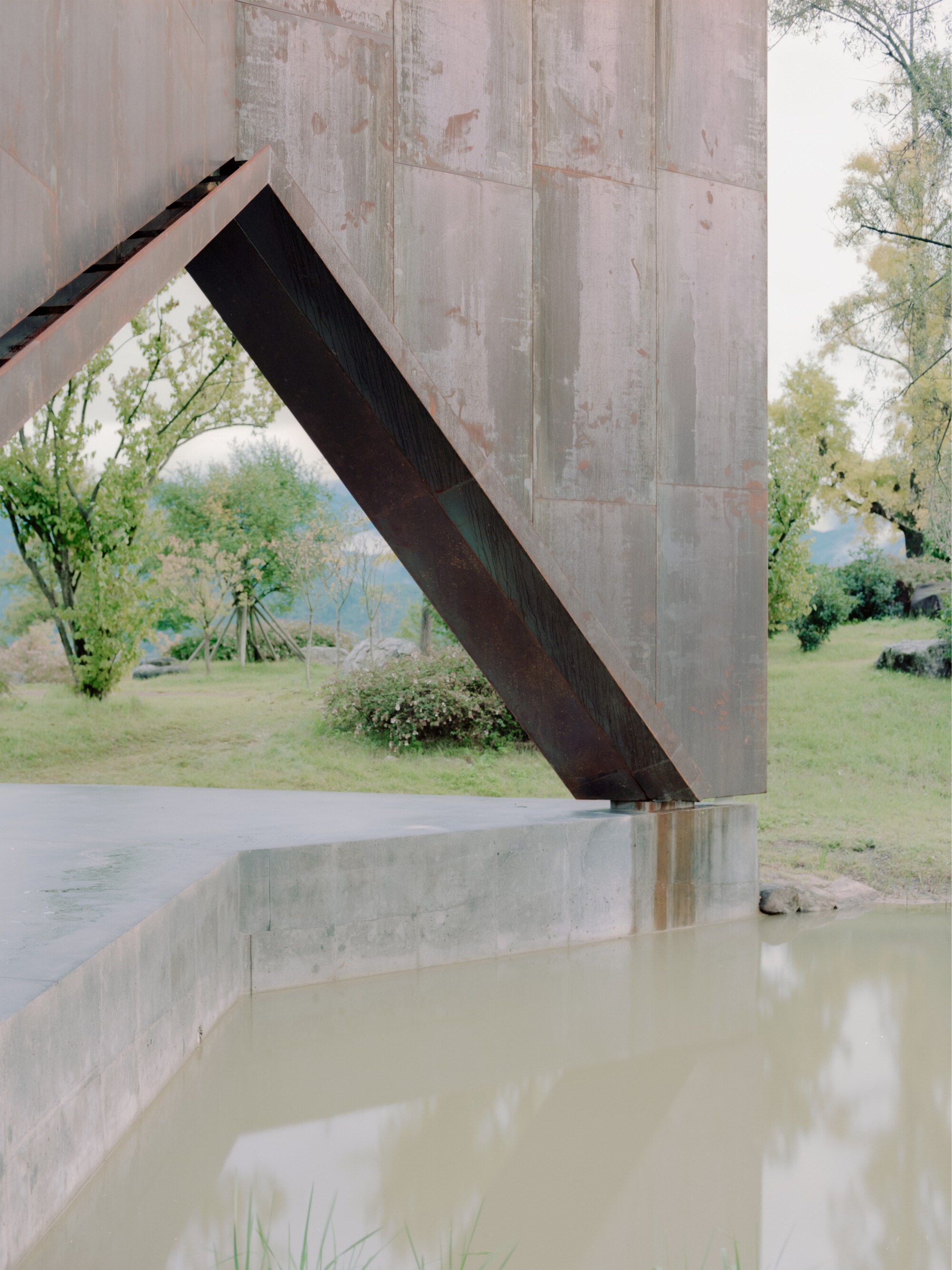 Angled steel brace connecting board-formed concrete column to ceiling near a reflecting pool