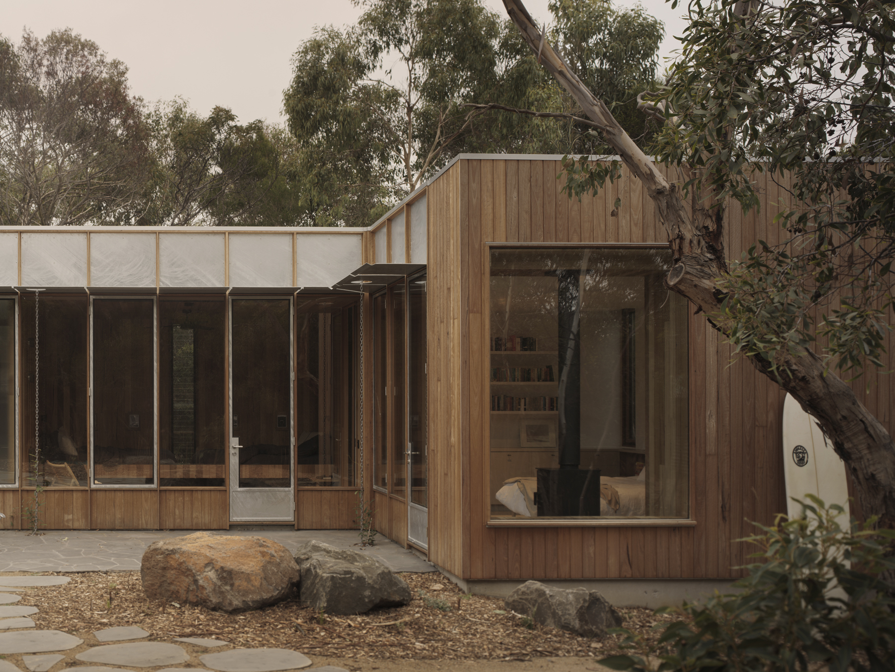 Timber-clad volumes with glazed openings and translucent upper panels arranged around a garden courtyard with boulders