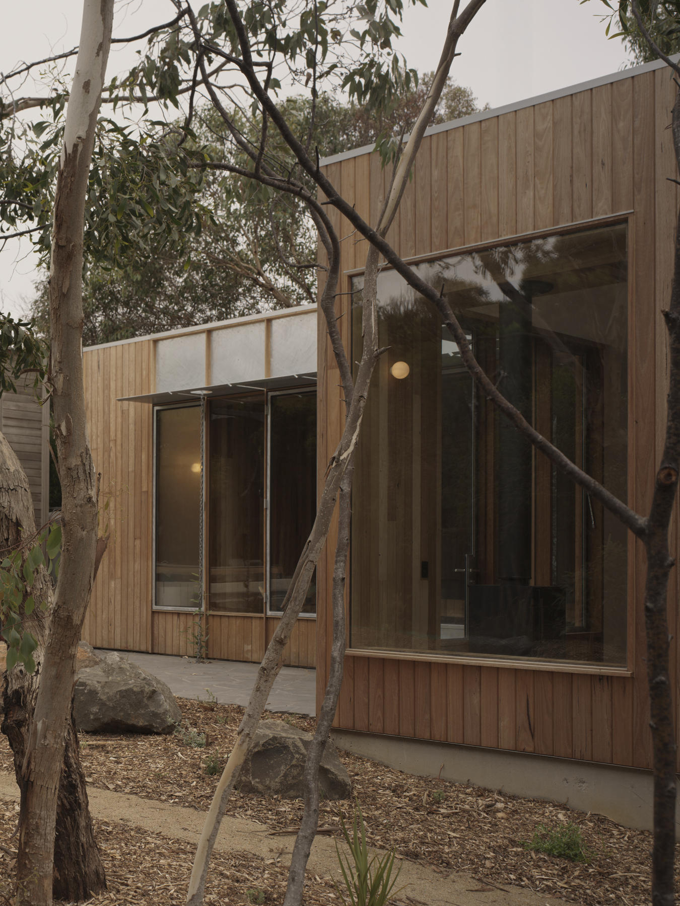 Vertical timber cladding and glazed facades framed by mature trees in an overcast garden setting
