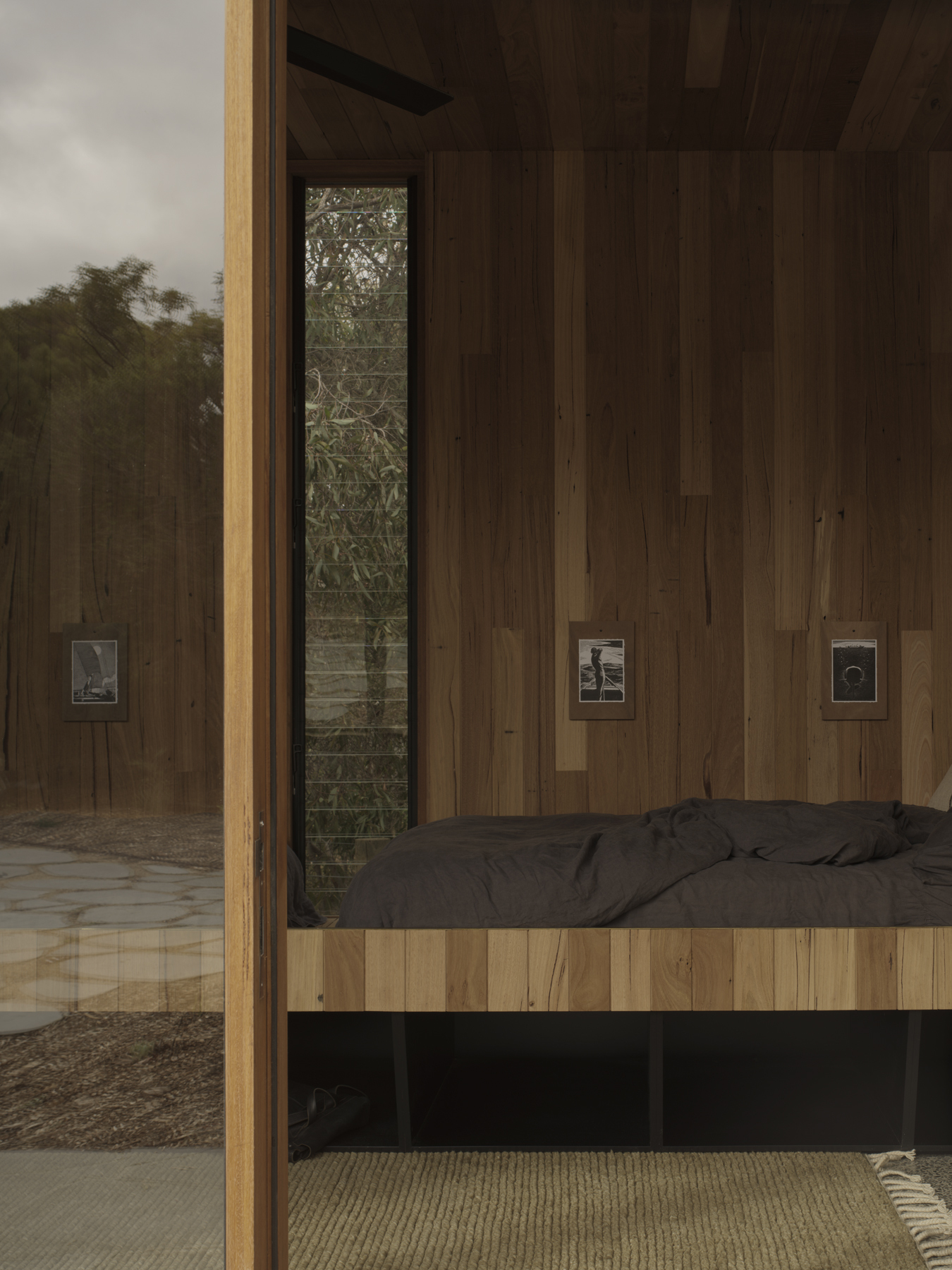 Interior bedroom with vertical timber wall cladding and built-in platform bed beside a glass door