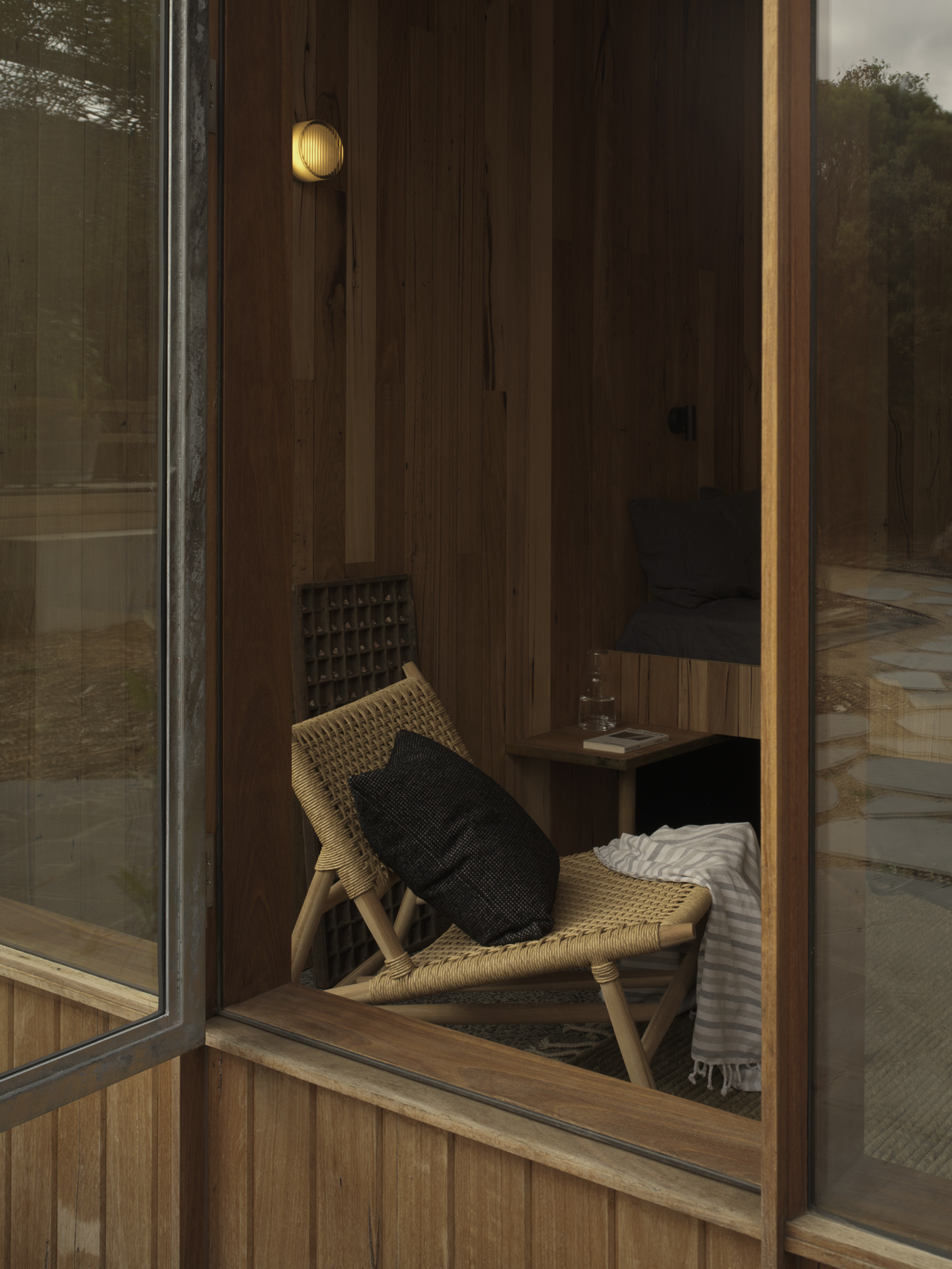 Woven chair against timber-paneled wall visible through glazed sliding door from exterior courtyard