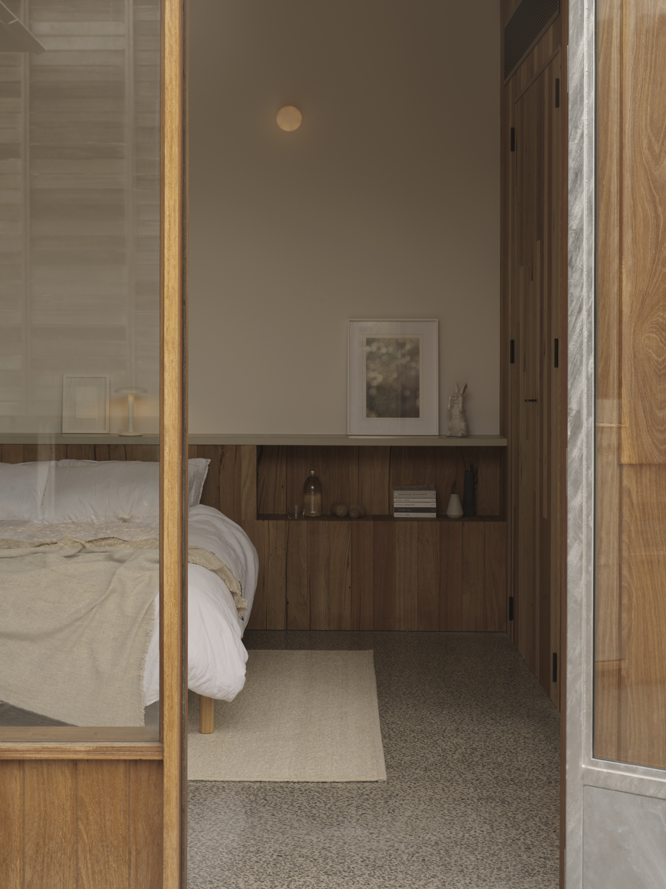 Bedroom alcove with built-in timber cabinetry and terrazzo flooring visible through glass partition