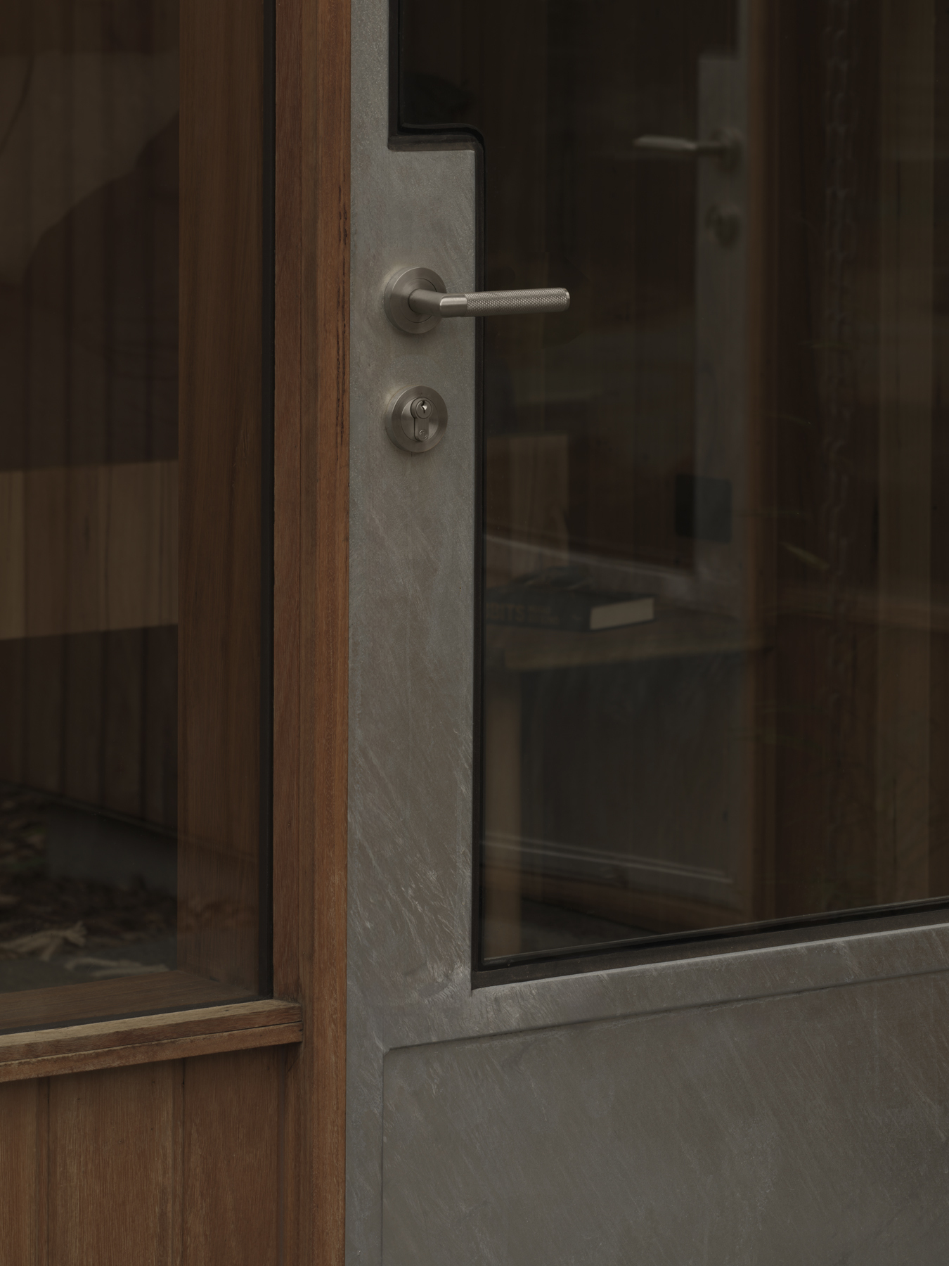 Timber and glass door with brushed metal lever handle and concrete frame edge