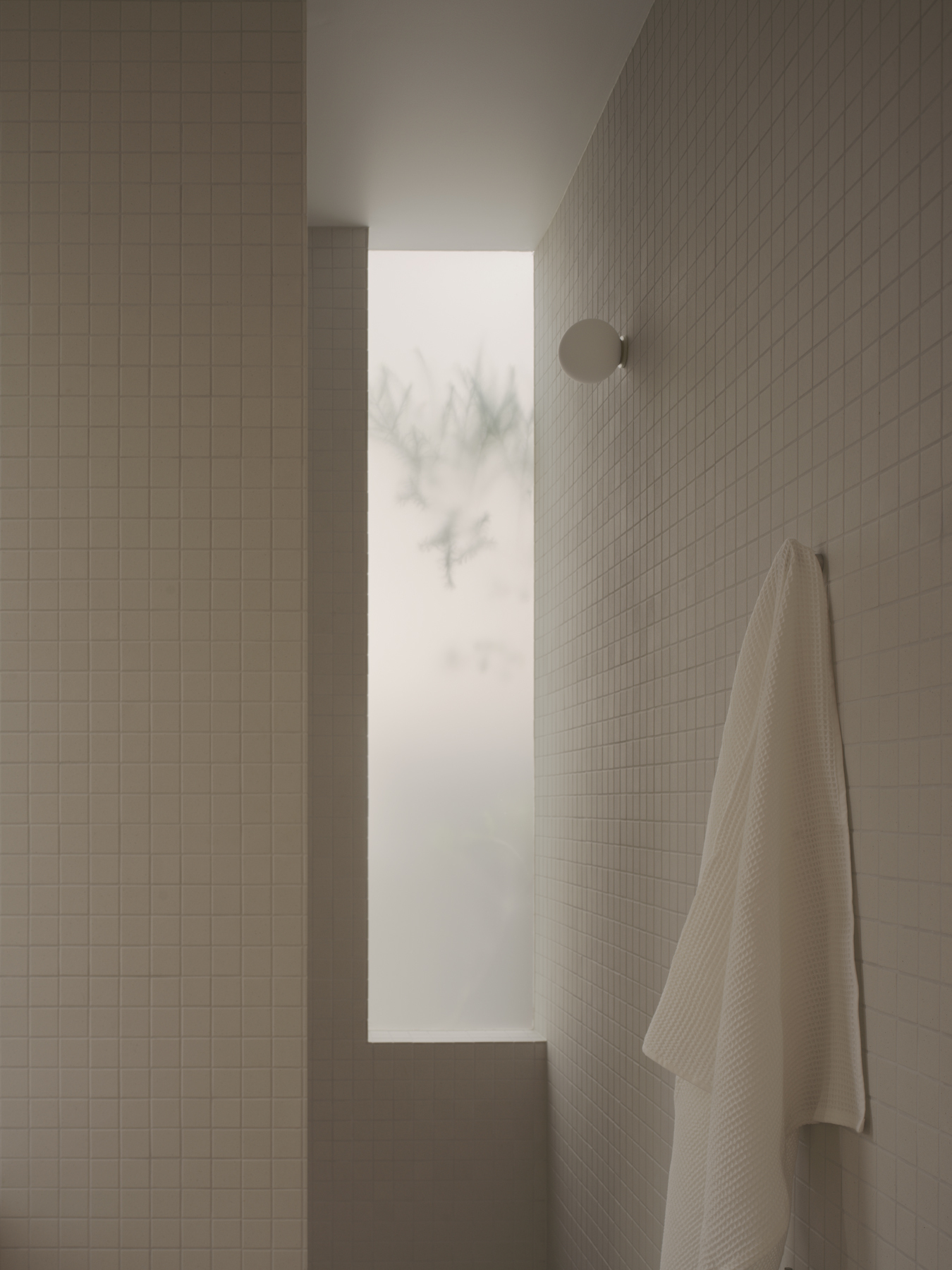 Tiled bathroom corner with narrow window framing winter trees in mist