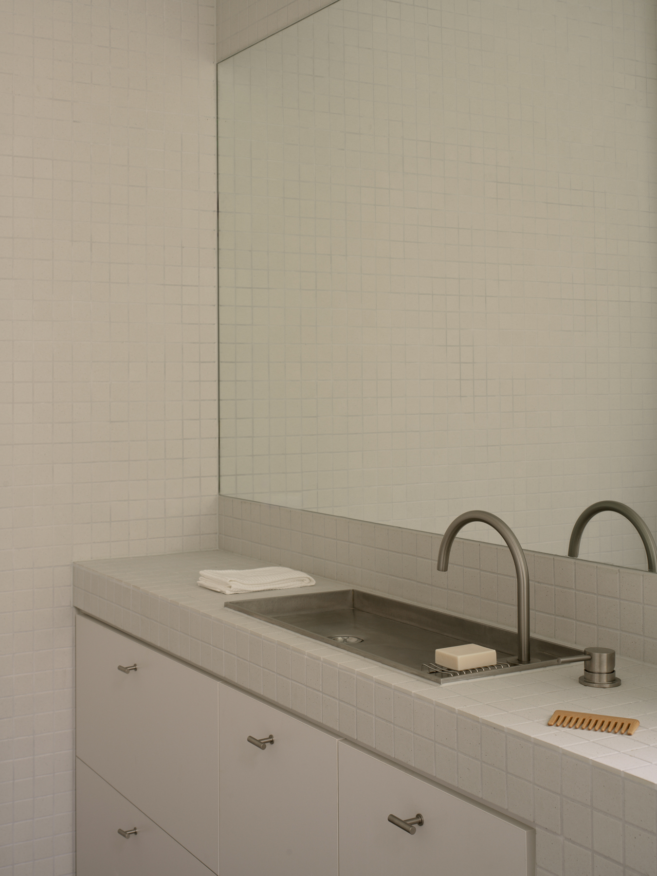 White tiled bathroom vanity with dual basins and integrated concrete countertop beneath a frameless mirror