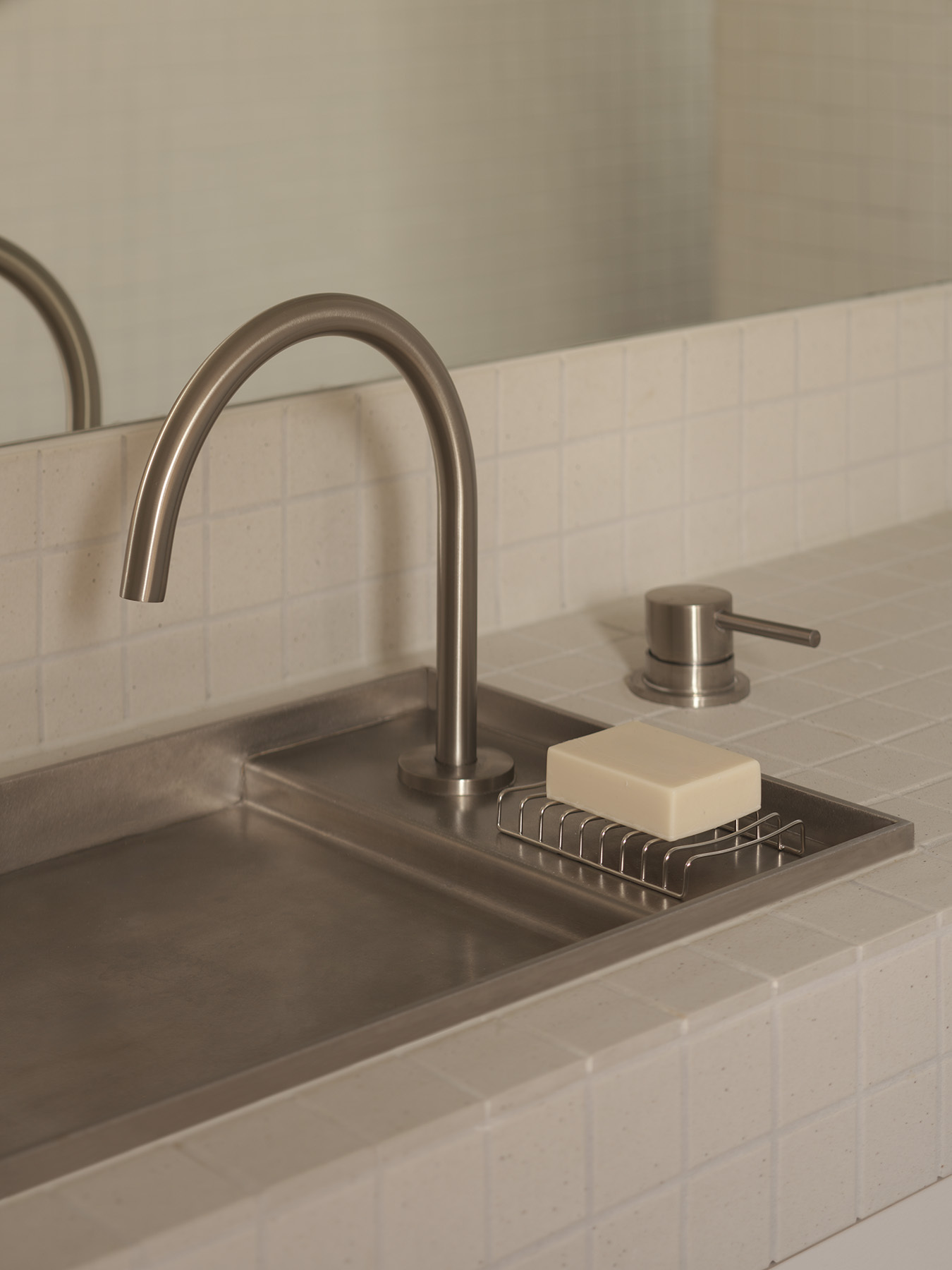 Close-up of brushed steel faucet and soap dish inset in concrete bathroom basin