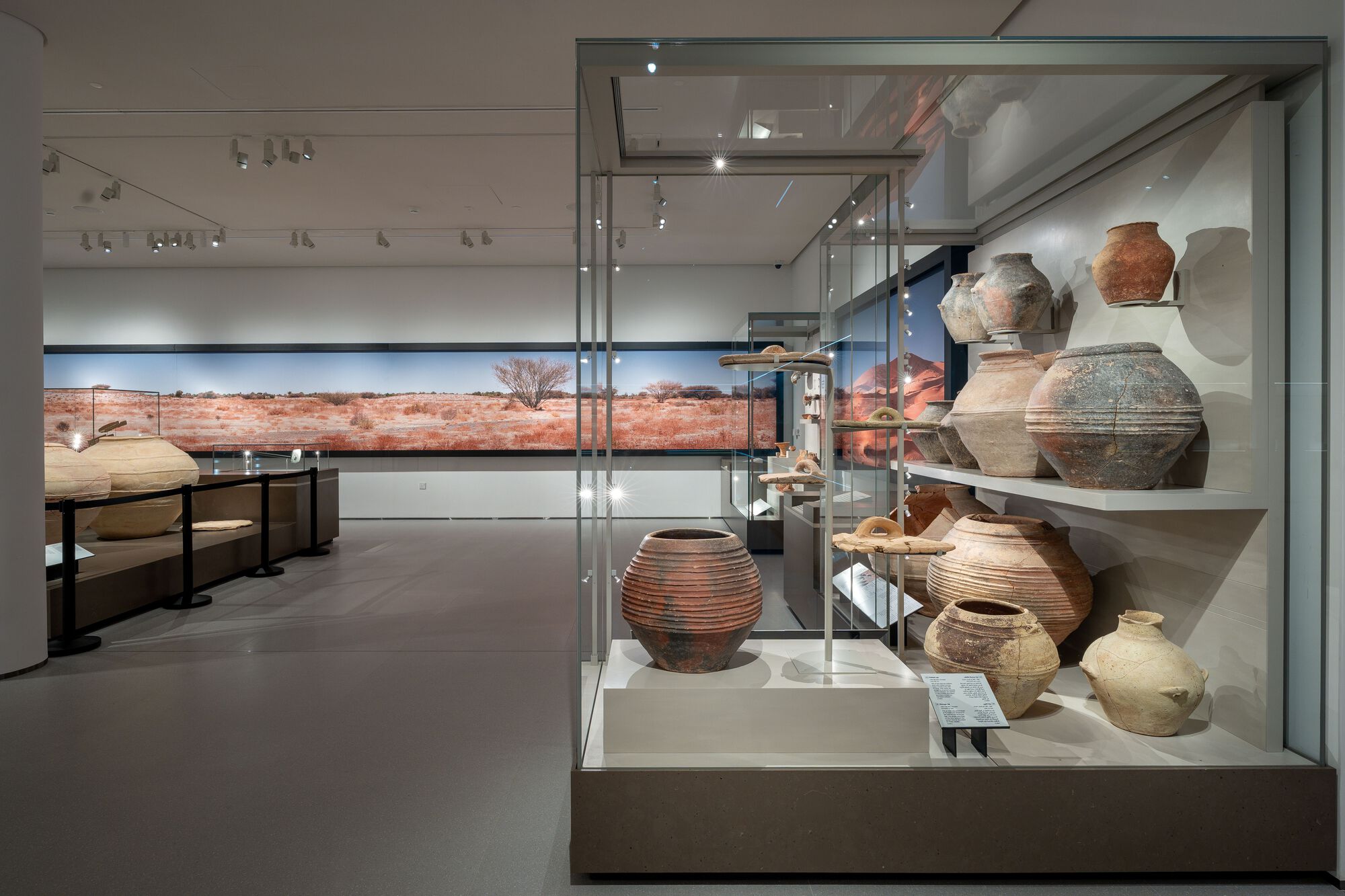 Glass display cases holding ceramic vessels with desert landscape visible through horizontal window