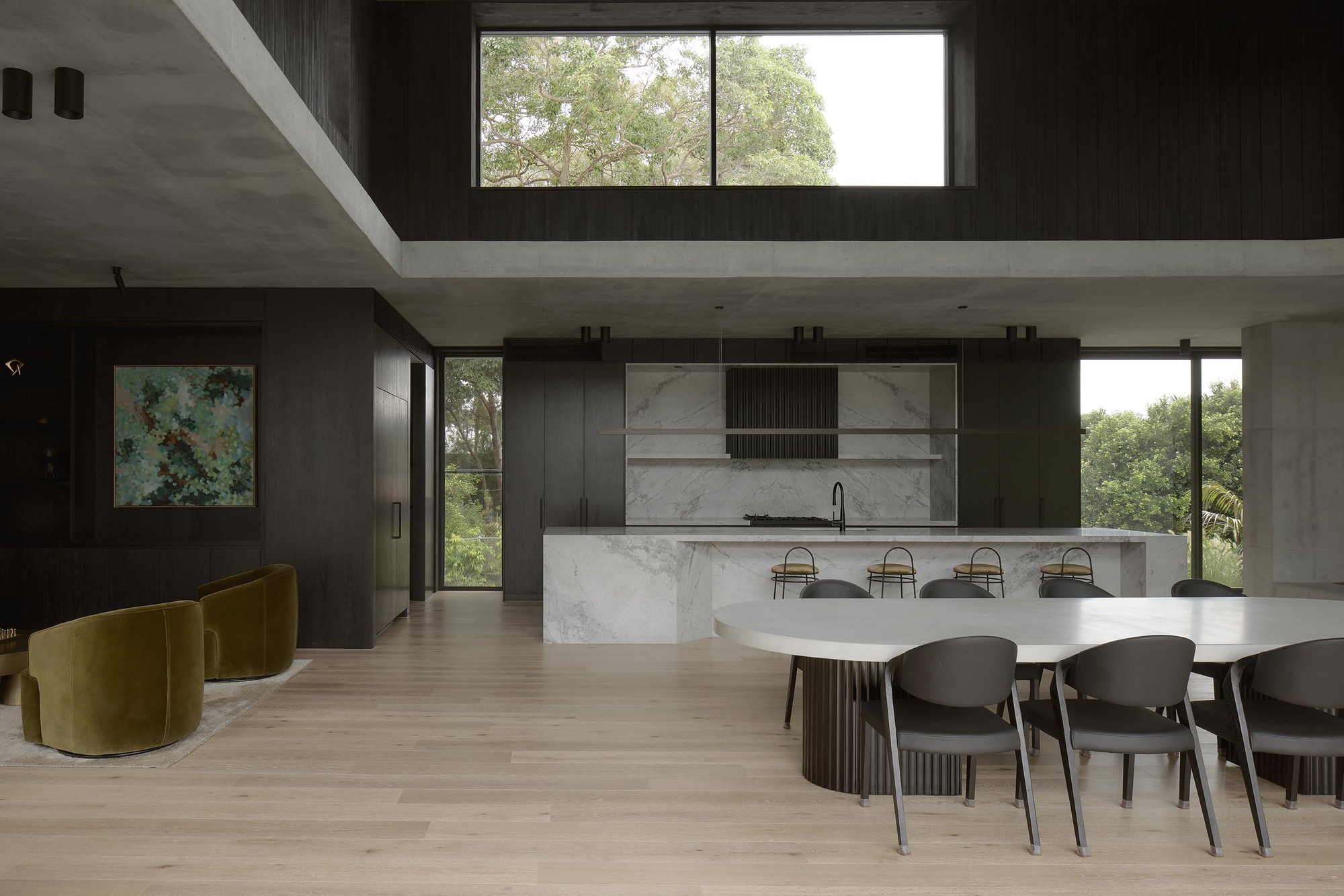Double-height living space with marble island, dining table and clerestory window overlooking trees