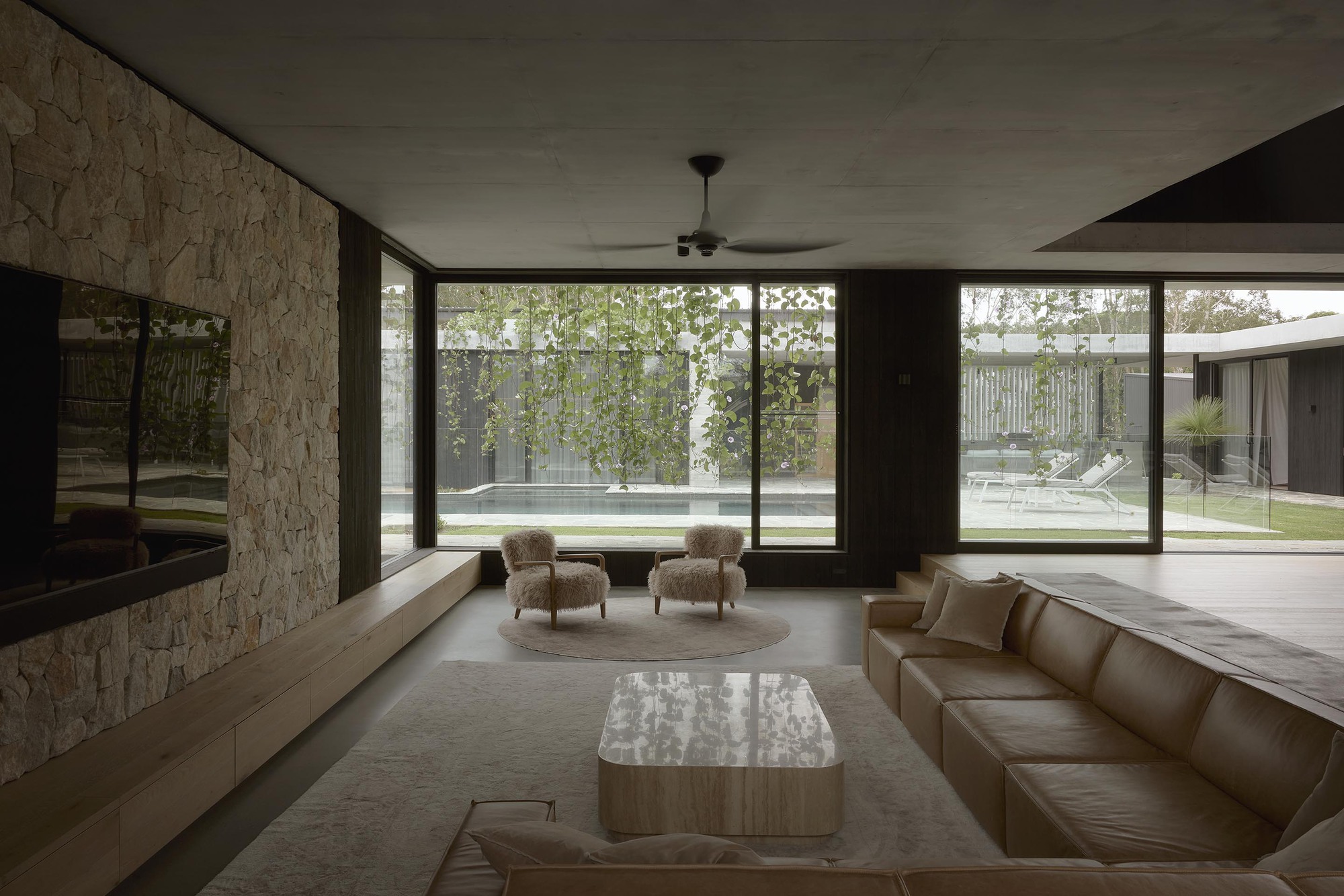 Sunken lounge with textured stone wall and floor-to-ceiling glazing opening to pool courtyard
