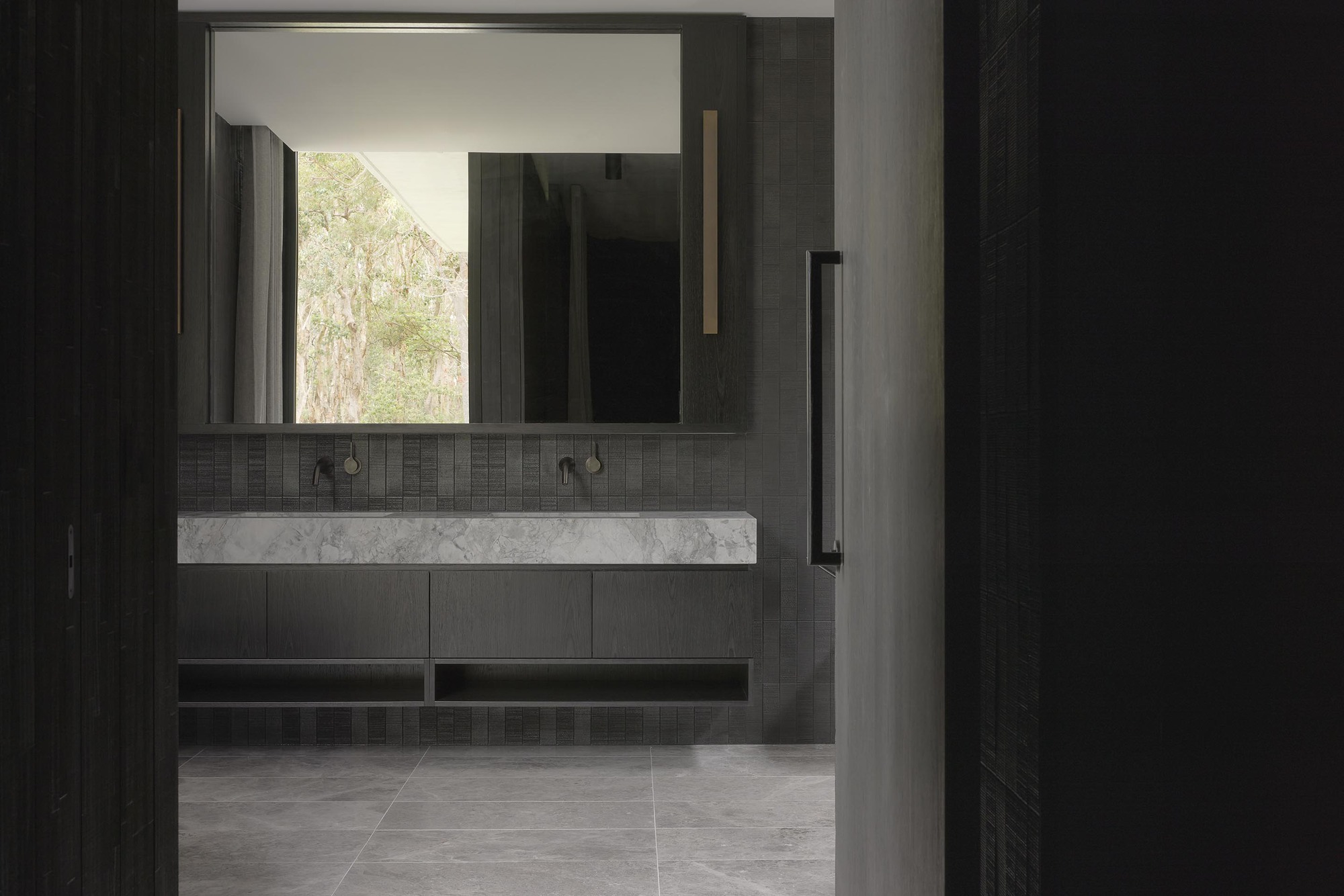 Bathroom vanity with marble countertop, dark tile and mirror reflecting trees outside