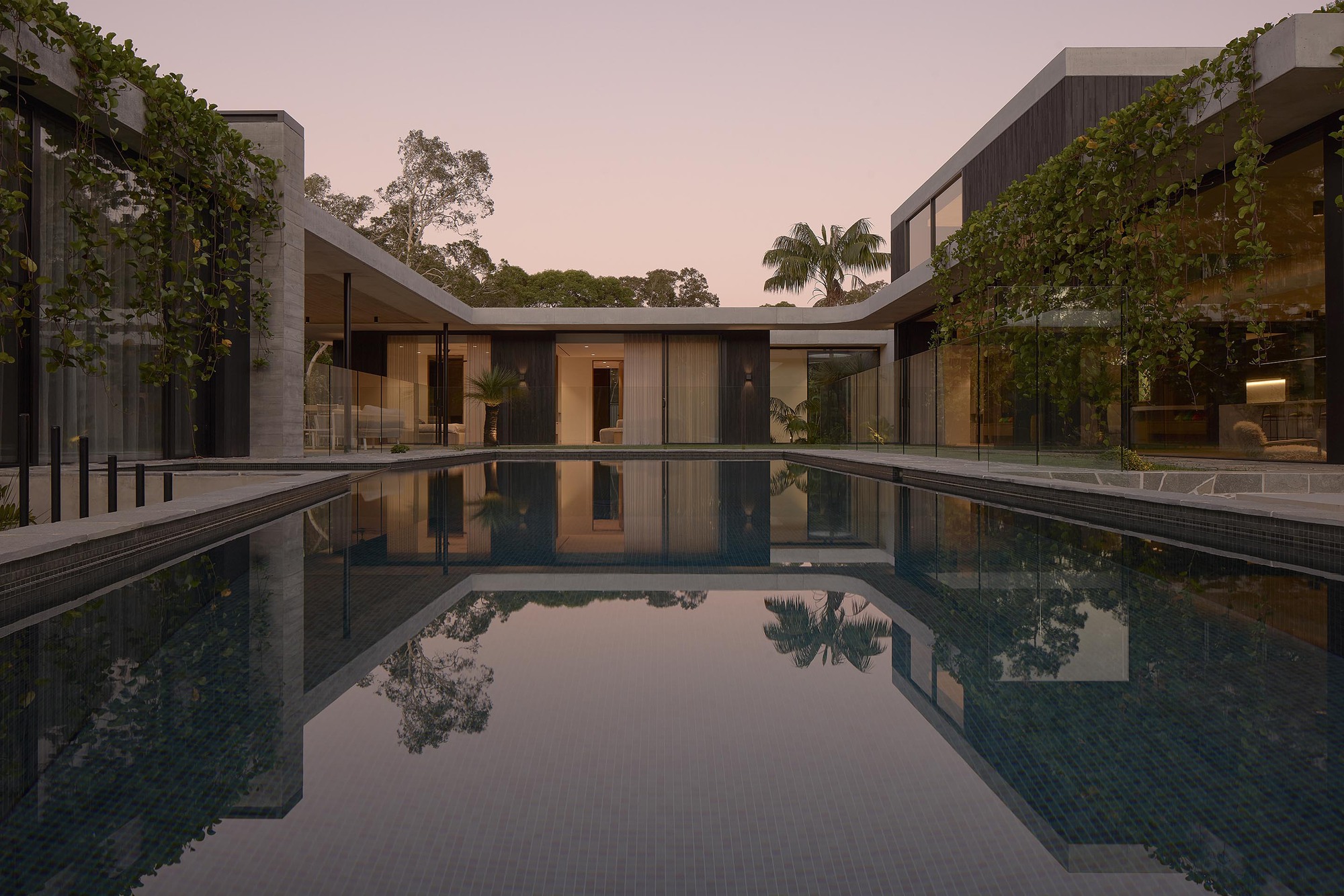 Courtyard pool reflecting glass pavilions and greenery at twilight