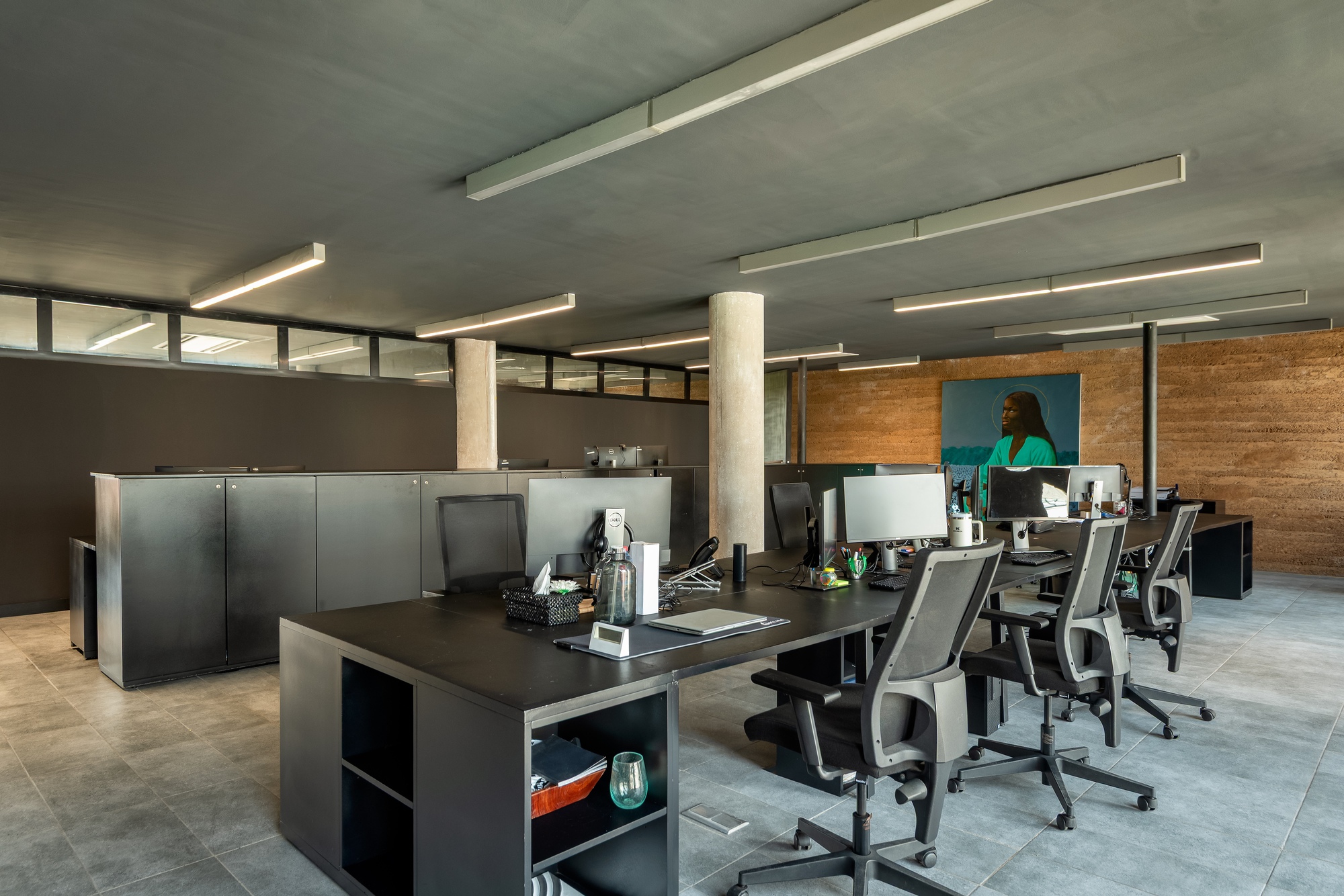 Open office space with concrete ceiling, linear lighting, and workstations beneath high clerestory windows