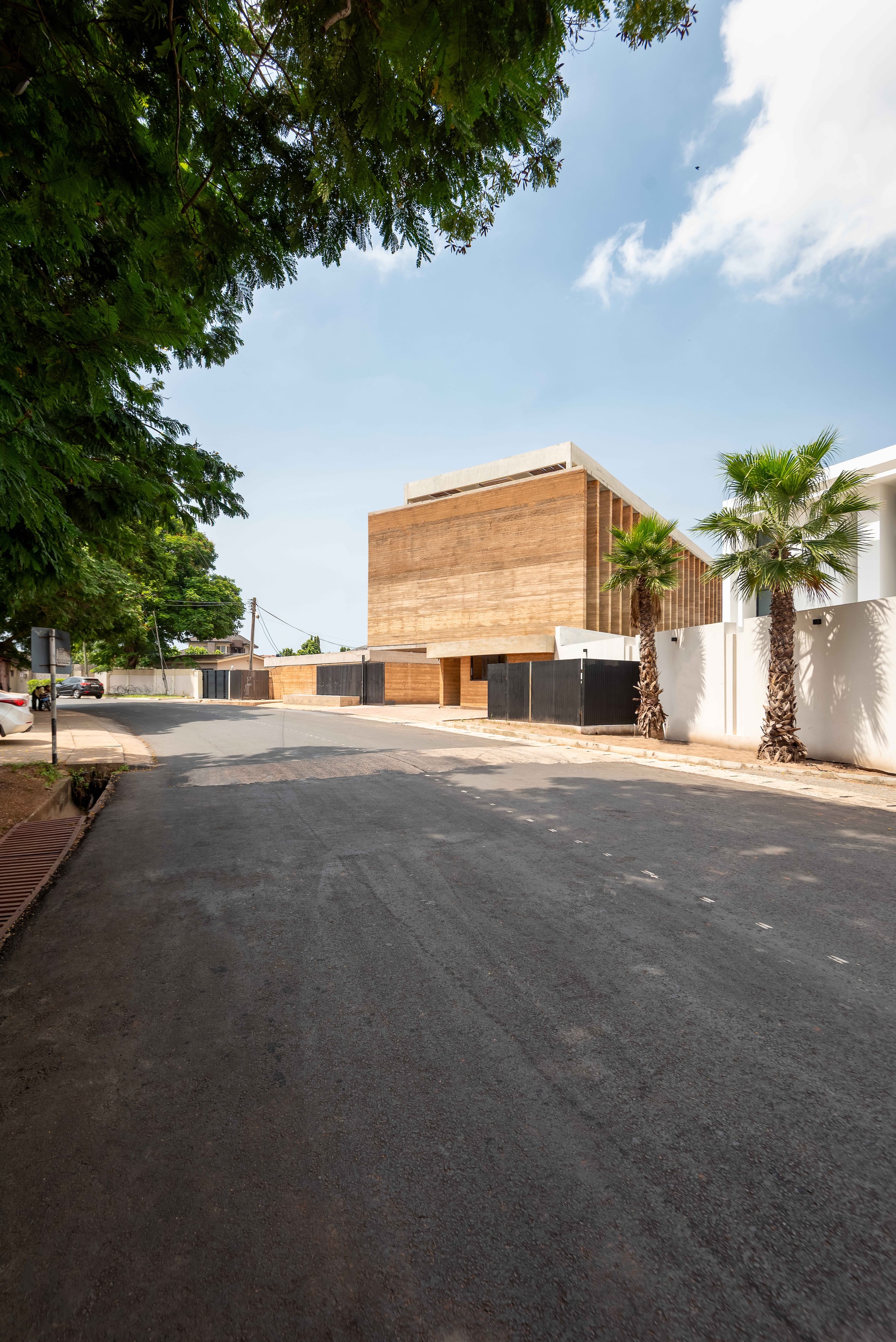 Street view of the layered rammed earth facade with vertical timber fins under afternoon sunlight