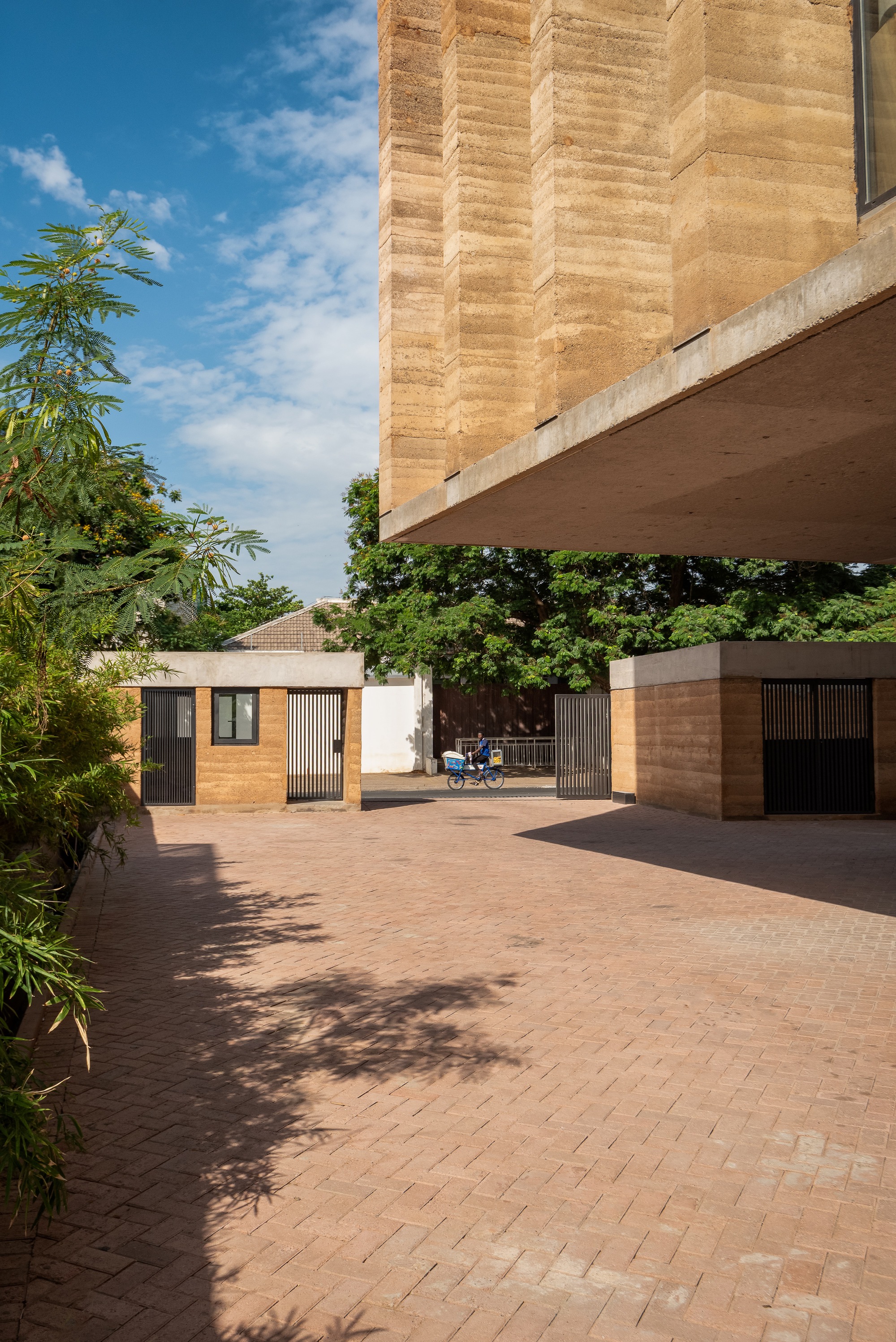 Paved courtyard beneath the cantilevered upper floor with motorcycle and tree shadows across terracotta pavers