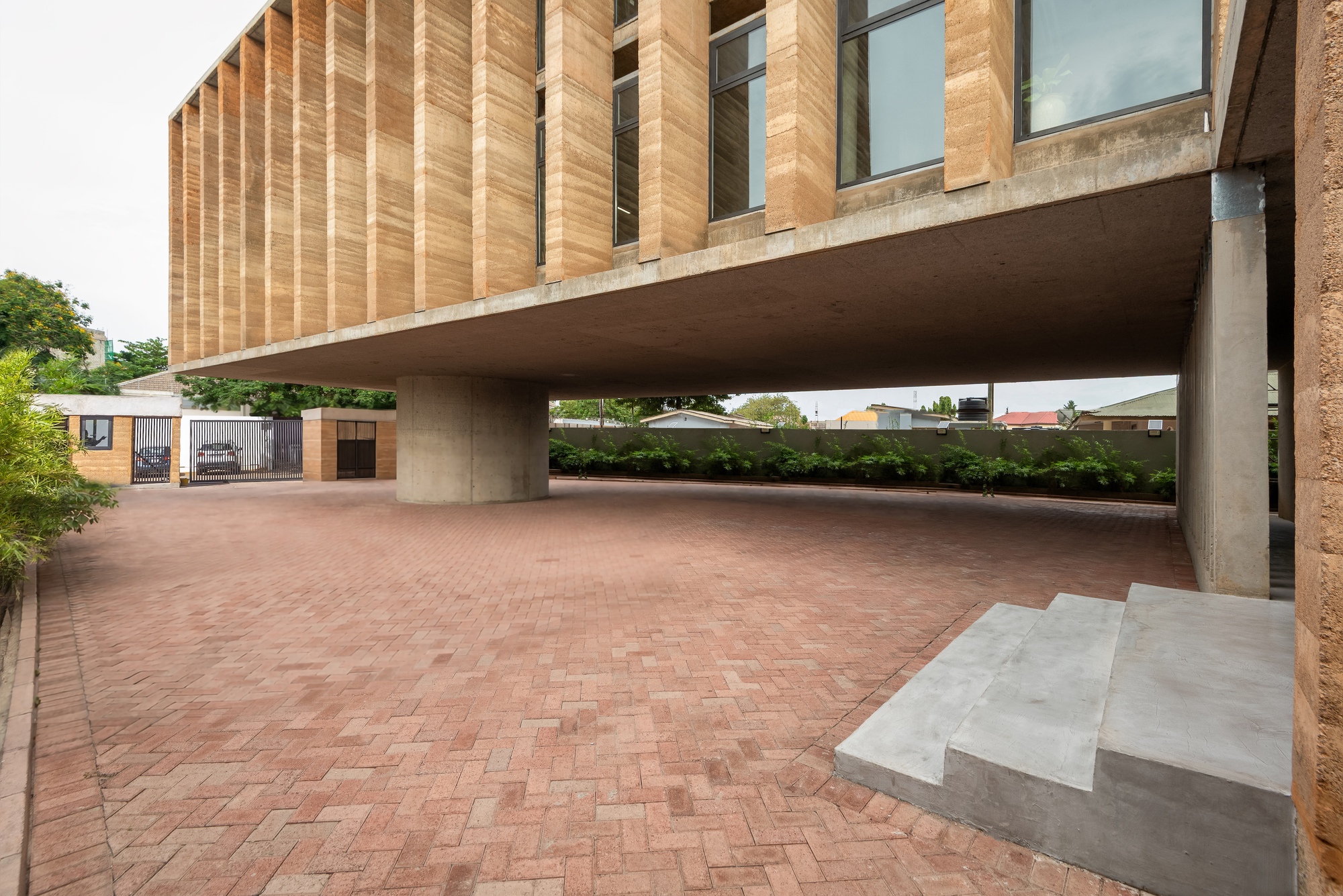 View across the brick courtyard showing the concrete slab hovering above on cylindrical supports