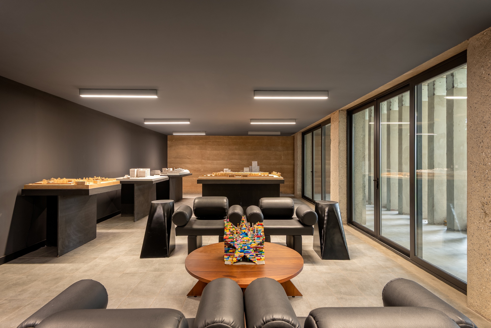 Studio workspace with model tables and lounge seating overlooking a glazed courtyard with vertical fins