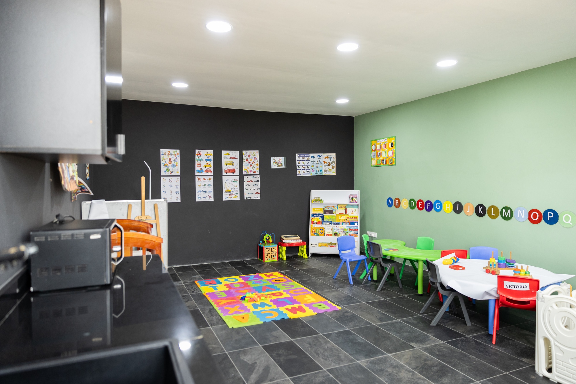 Children's playroom with pale green and charcoal walls, alphabet letters, and colorful furniture on tile flooring
