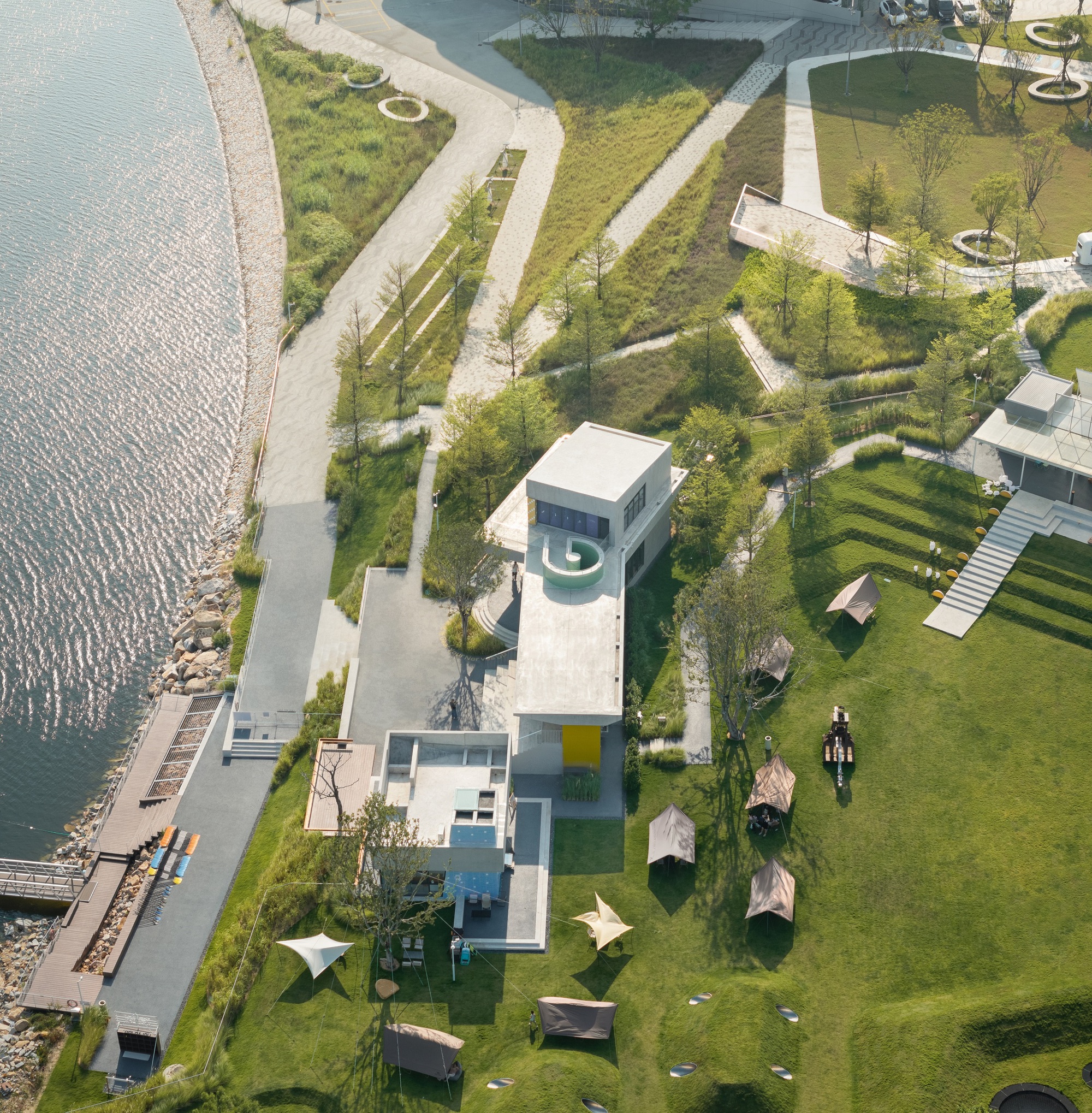 Aerial view of white pavilions surrounded by curved terraced lawn and waterfront dock with kayakers