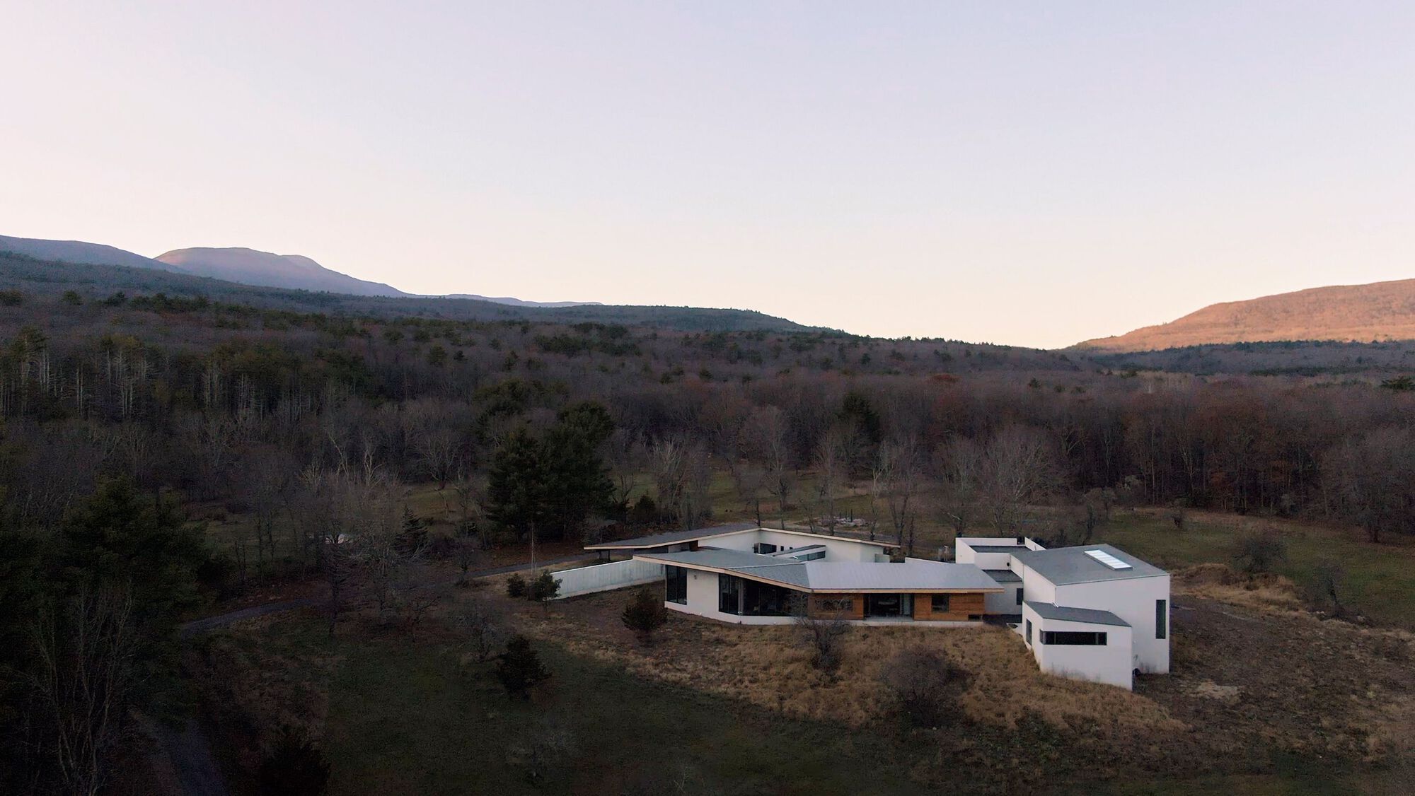 Aerial view of the low-slung residence with metal roofs nestled among bare trees and rolling hills