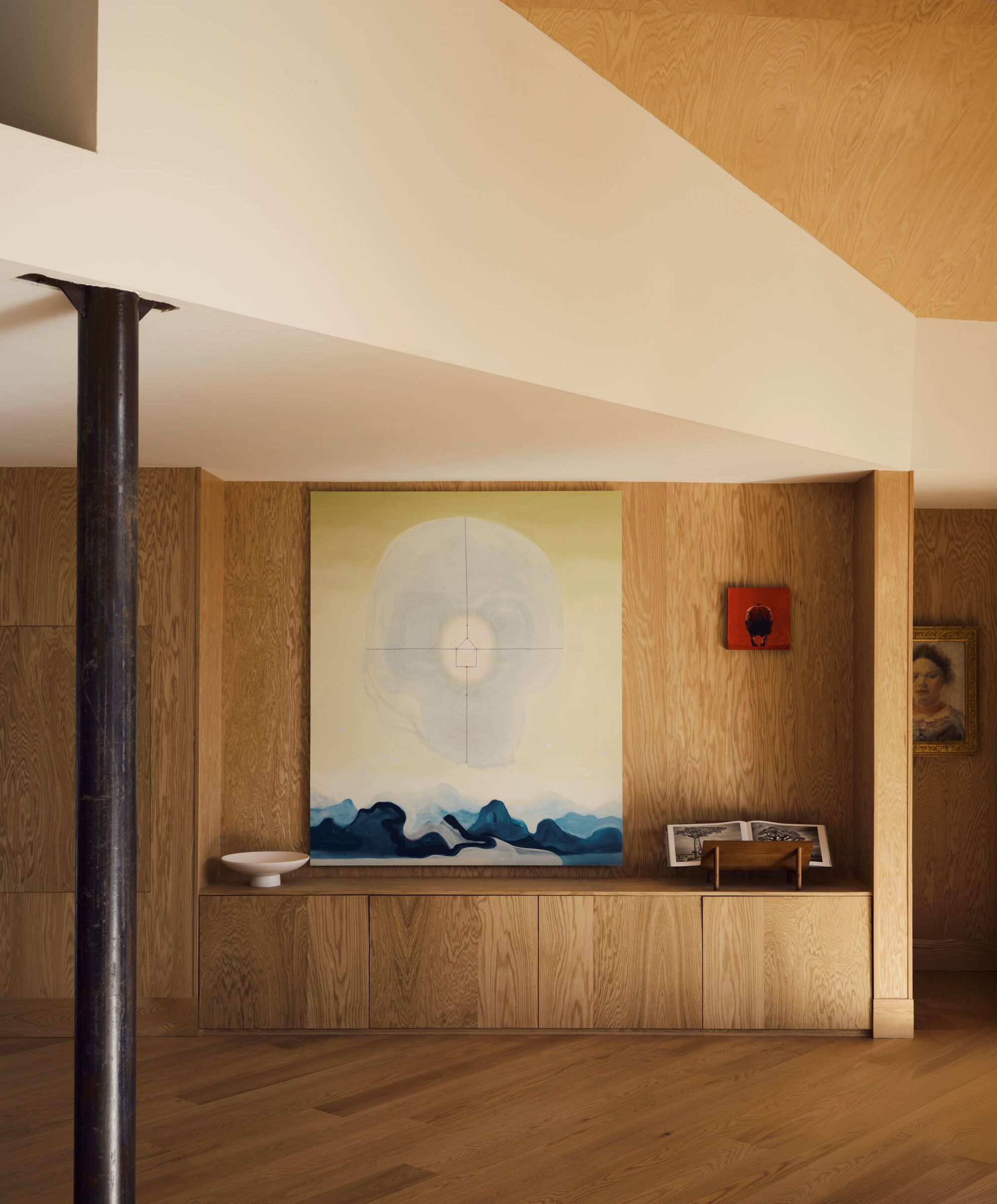 Oak credenza below a large artwork flanked by a slender black steel column in natural light