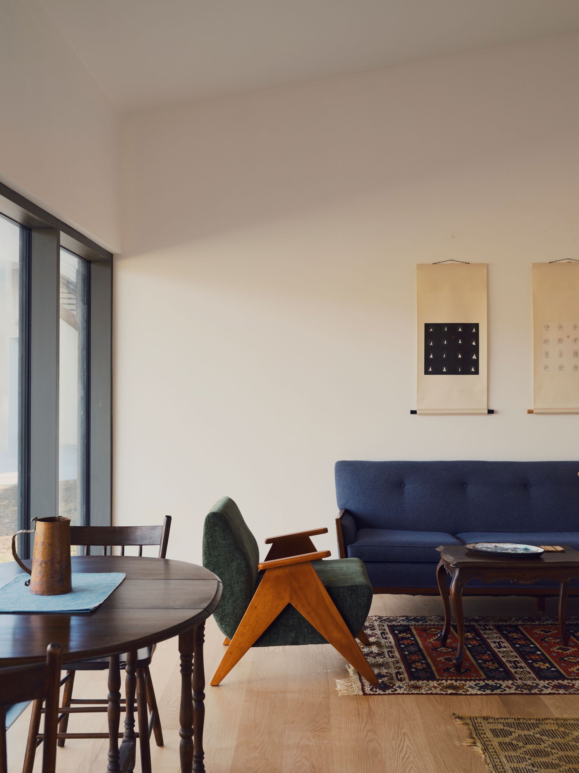 Living area with round dining table, upholstered chairs, floor-to-ceiling windows, and hanging scrolls on the wall