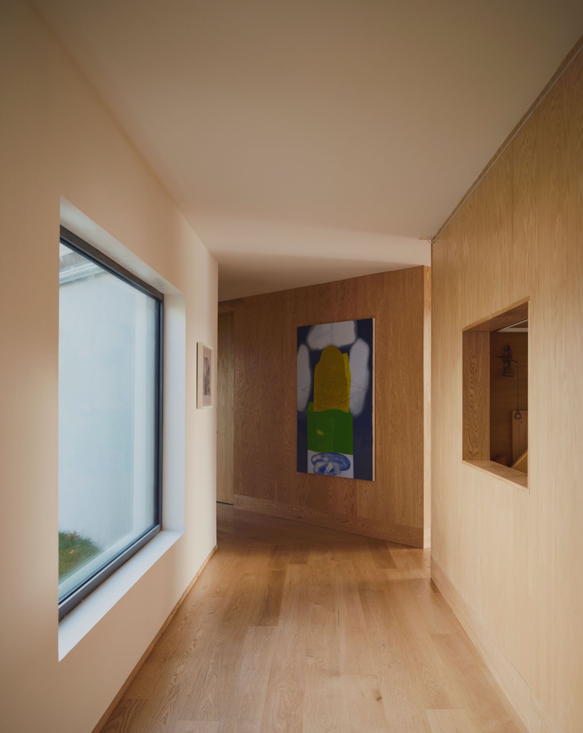 Interior hallway with oak flooring, wood-paneled walls, recessed niche, and framed artwork at the end