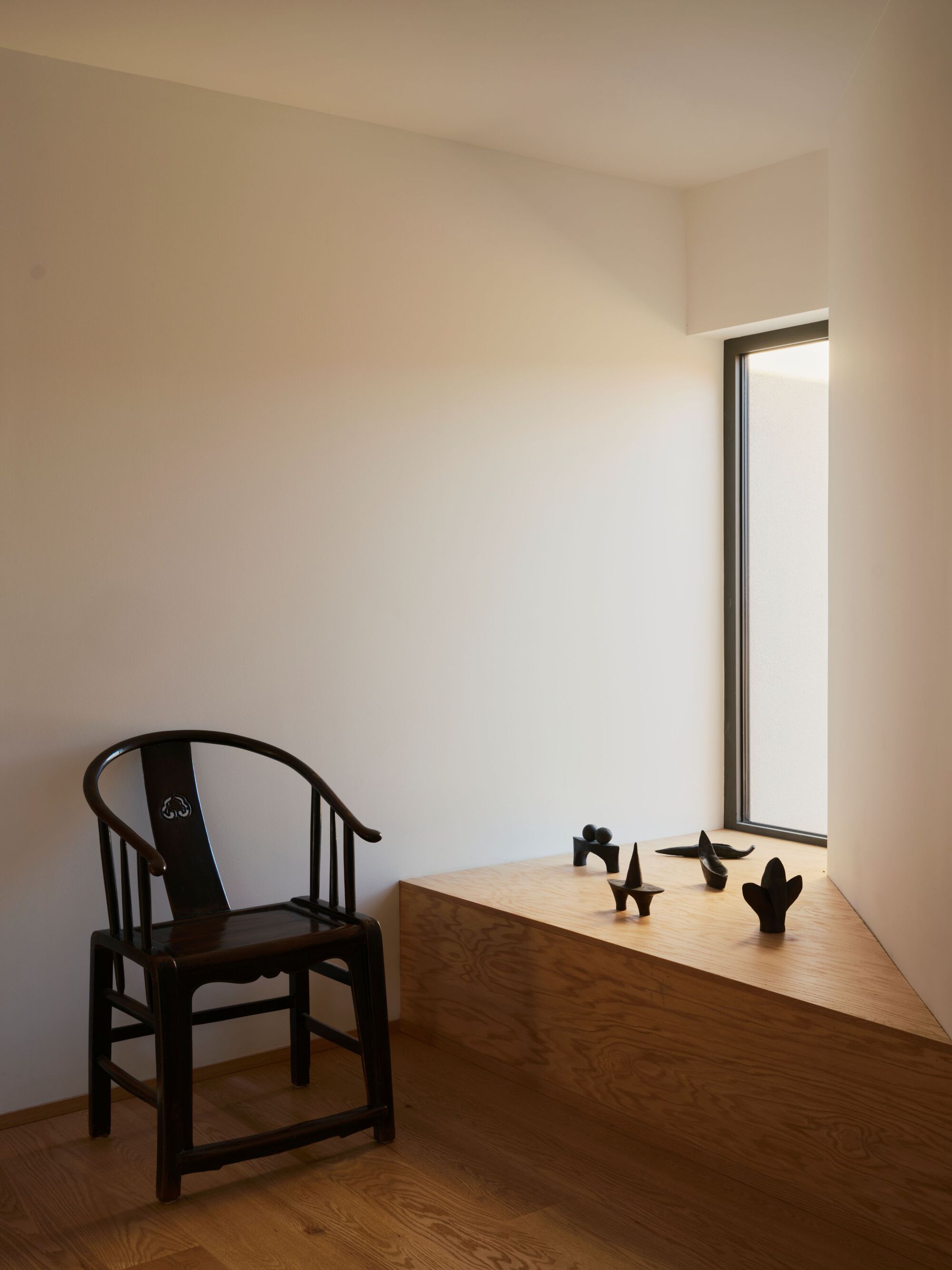 Built-in desk beside a tall narrow window with small sculptures arranged on the wood surface