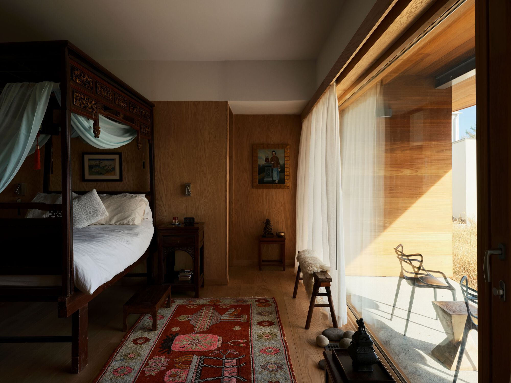 Bedroom with carved canopy bed and floor-to-ceiling glass opening to a sunlit terrace