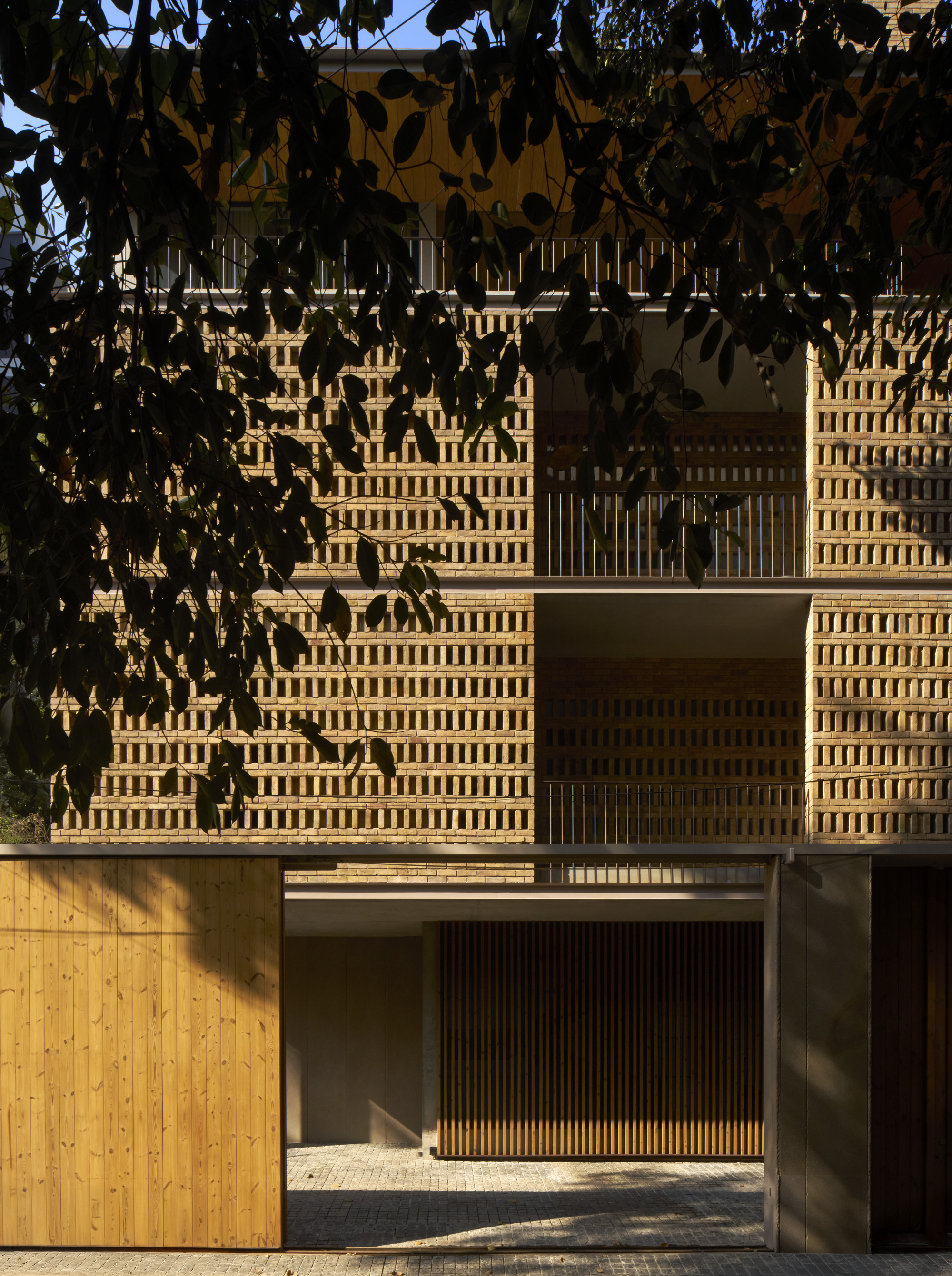 Entry view showing perforated brick screen walls and timber base filtered by tree shadow