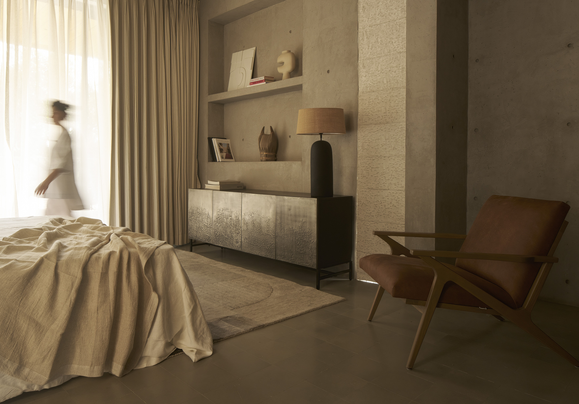 Bedroom with floating shelves and person passing through soft natural light from sheer curtains