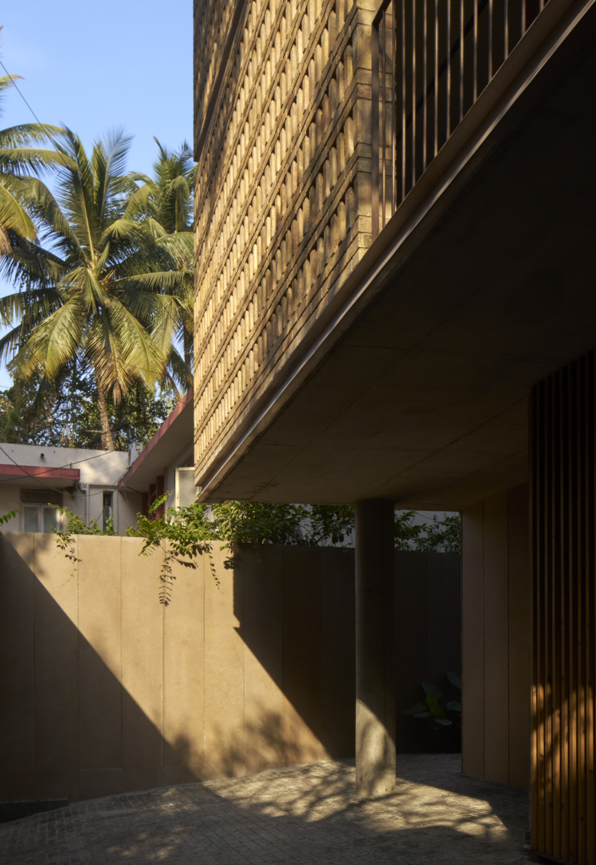 Entry courtyard with smooth concrete wall and perforated brick screen above framed by palm trees