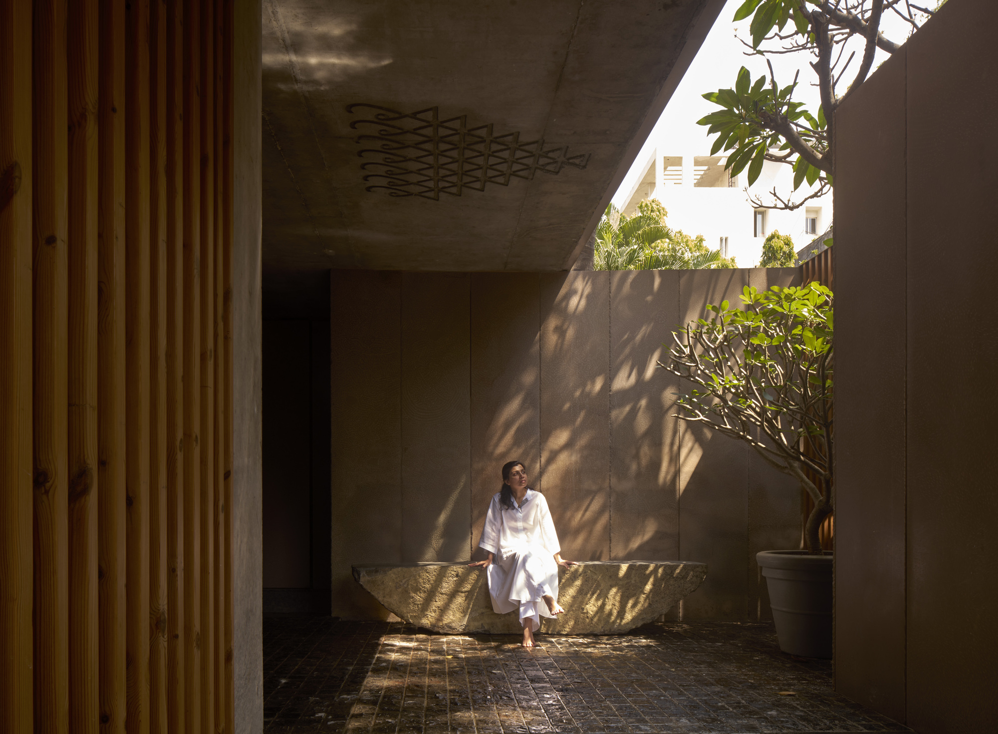 Ground floor courtyard with concrete soffit featuring geometric pattern and person seated on stone bench